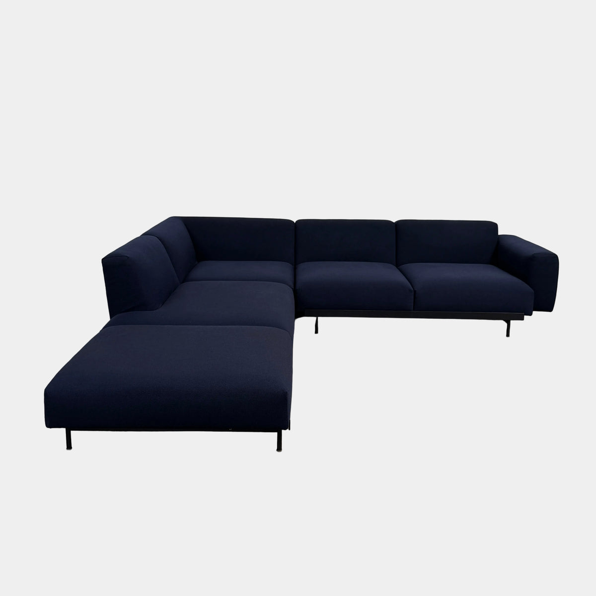 The Muuto Outline 3 Piece Sectional Sofa by Muuto features a dark blue fabric upholstery in a sleek, L-shaped design with low backrests and black legs, echoing the clean lines of contemporary architecture. The sectional stands out beautifully against a plain white background.