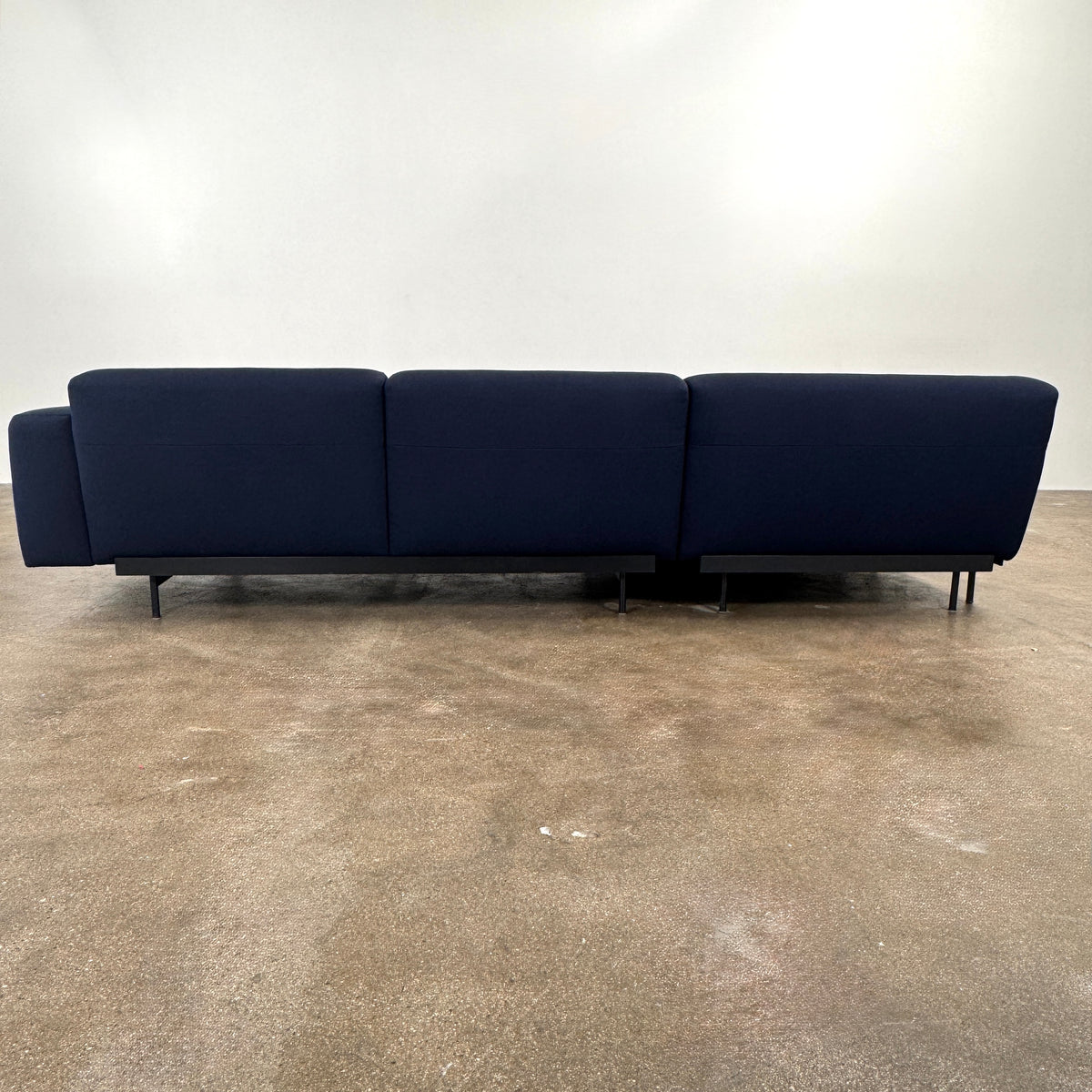 The Muuto Outline 3 Piece Sectional Sofa by Muuto features a dark blue fabric upholstery in a sleek, L-shaped design with low backrests and black legs, echoing the clean lines of contemporary architecture. The sectional stands out beautifully against a plain white background.