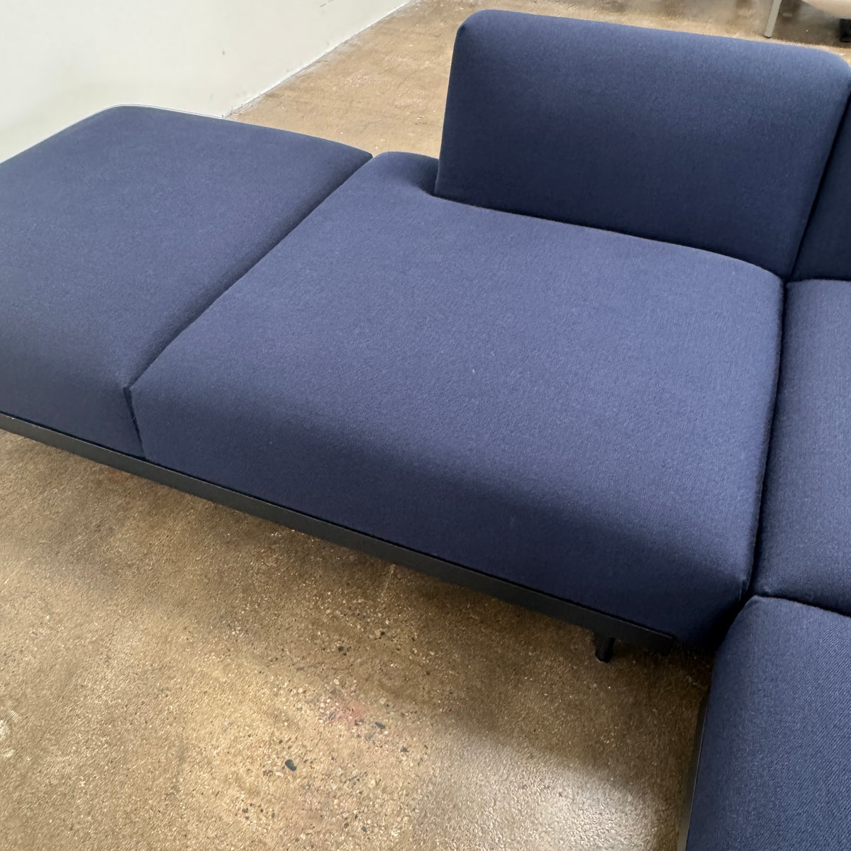The Muuto Outline 3 Piece Sectional Sofa by Muuto features a dark blue fabric upholstery in a sleek, L-shaped design with low backrests and black legs, echoing the clean lines of contemporary architecture. The sectional stands out beautifully against a plain white background.