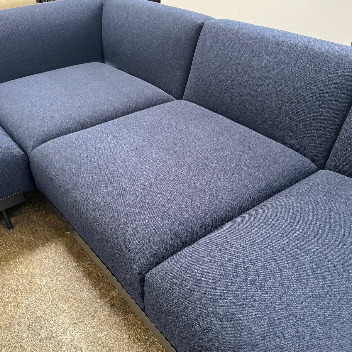 The Muuto Outline 3 Piece Sectional Sofa by Muuto features a dark blue fabric upholstery in a sleek, L-shaped design with low backrests and black legs, echoing the clean lines of contemporary architecture. The sectional stands out beautifully against a plain white background.