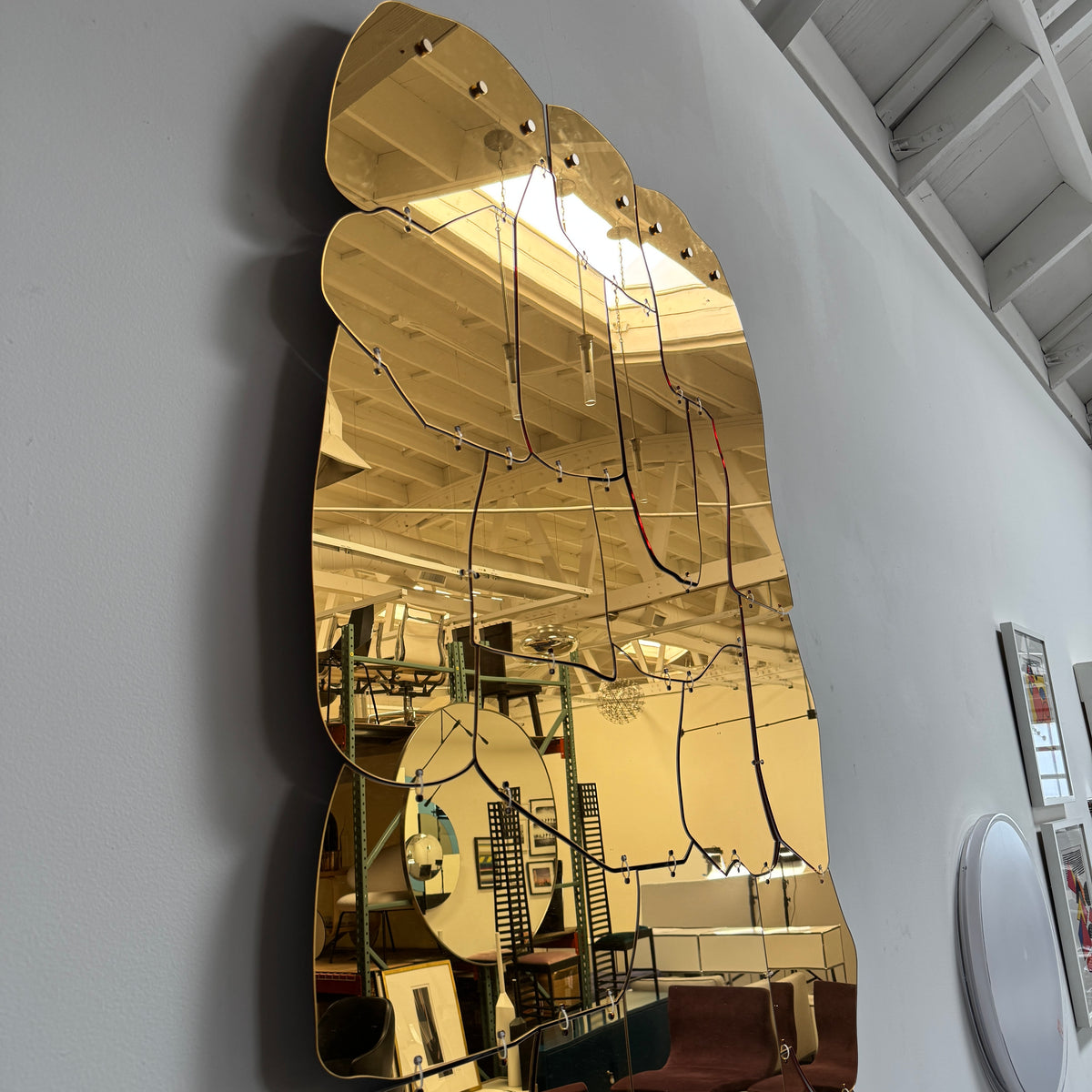 The Edra Miraggio Mirror by Edra features irregular, gold-toned metal panels with visible fasteners, mounted on a white background to highlight its artisanal craftsmanship.
