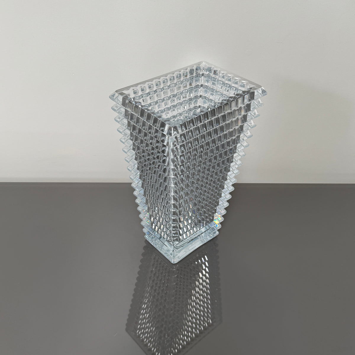 The Baccarat Eye Vase by Baccarat features clear glass with a geometric textured design, shown on a white pedestal and plain white background.