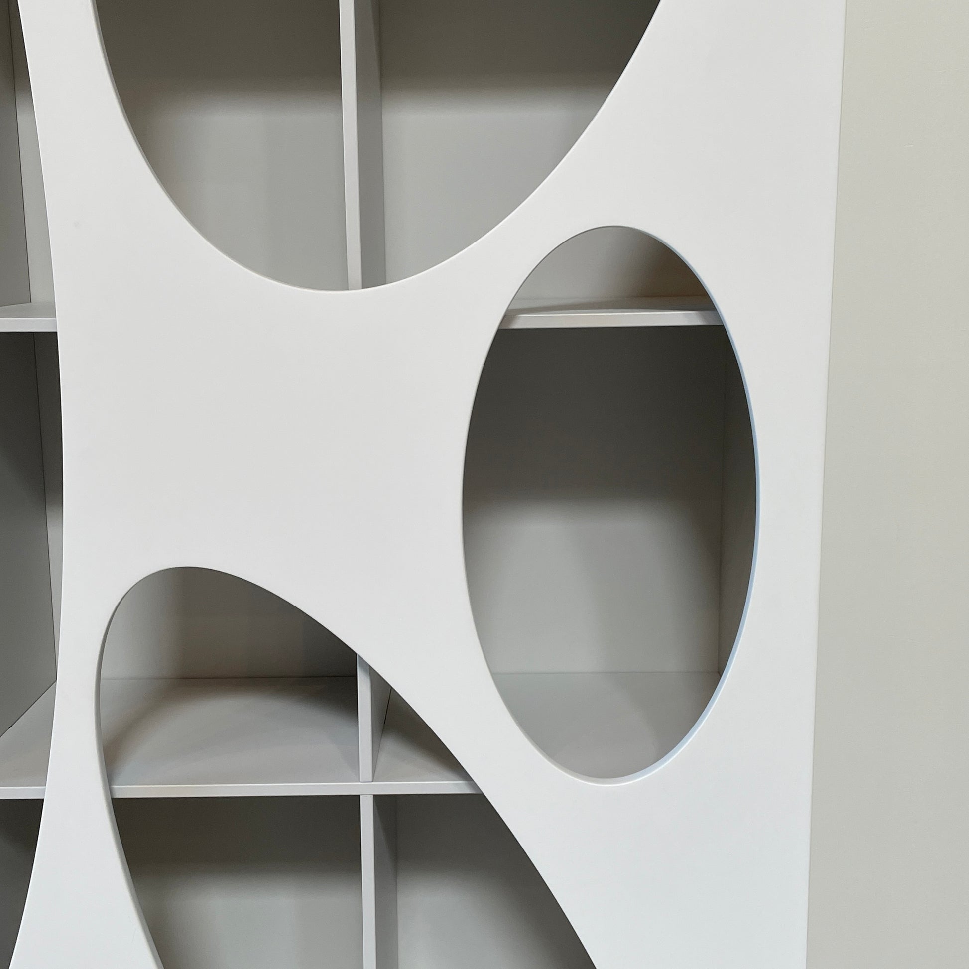 The Roche Bobois Denia Bookcase is a white bookshelf characterized by its abstract design, featuring multiple irregular oval cutouts, nine internal compartments, and integrated LED lighting, reminiscent of ROCHE BOBOIS styling.