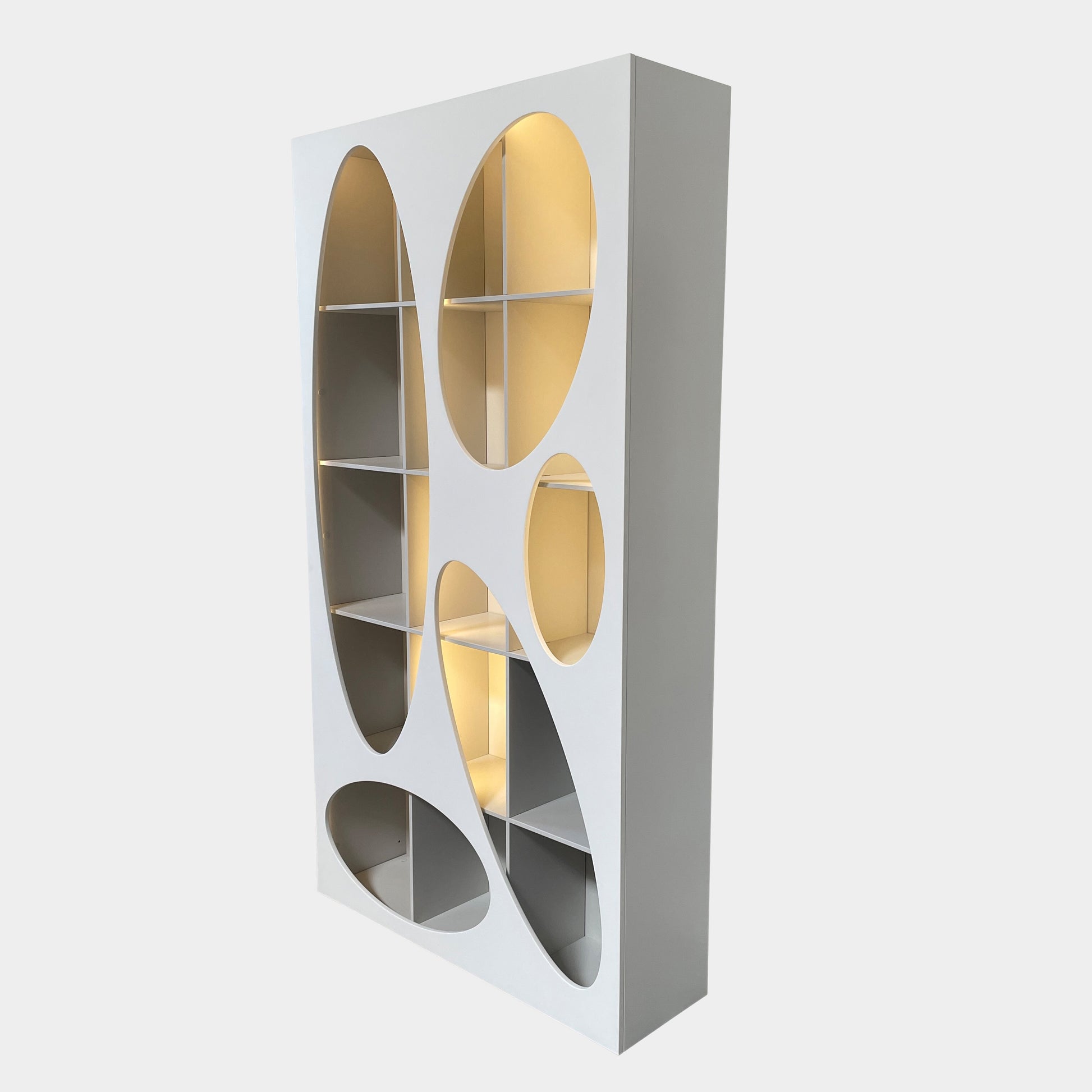 The Roche Bobois Denia Bookcase is a white bookshelf characterized by its abstract design, featuring multiple irregular oval cutouts, nine internal compartments, and integrated LED lighting, reminiscent of ROCHE BOBOIS styling.
