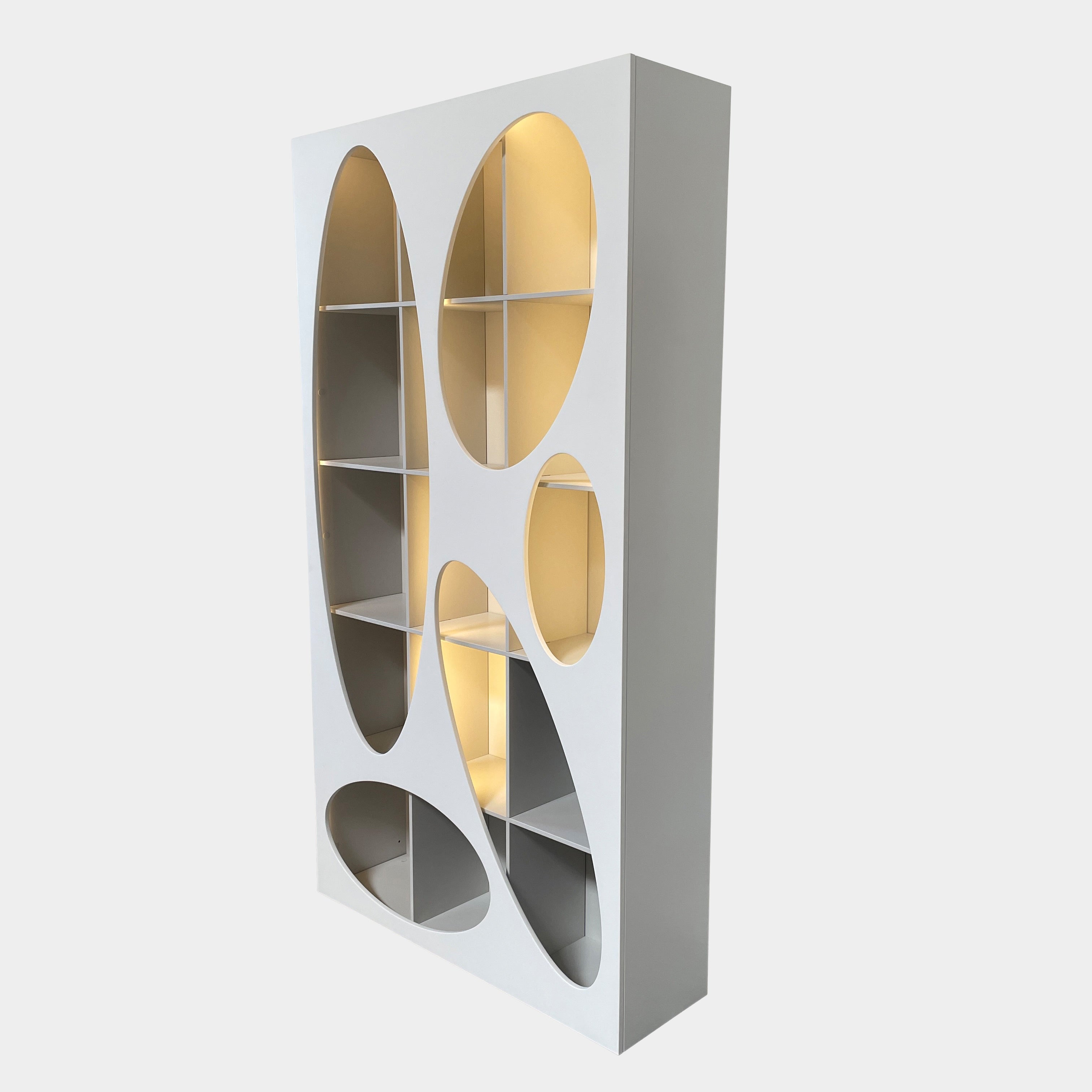 The Roche Bobois Denia Bookcase is a white bookshelf characterized by its abstract design, featuring multiple irregular oval cutouts, nine internal compartments, and integrated LED lighting, reminiscent of ROCHE BOBOIS styling.