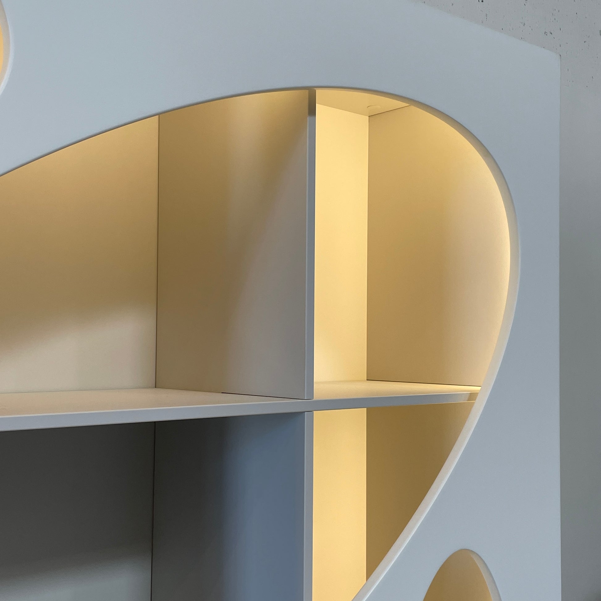 The Roche Bobois Denia Bookcase is a white bookshelf characterized by its abstract design, featuring multiple irregular oval cutouts, nine internal compartments, and integrated LED lighting, reminiscent of ROCHE BOBOIS styling.