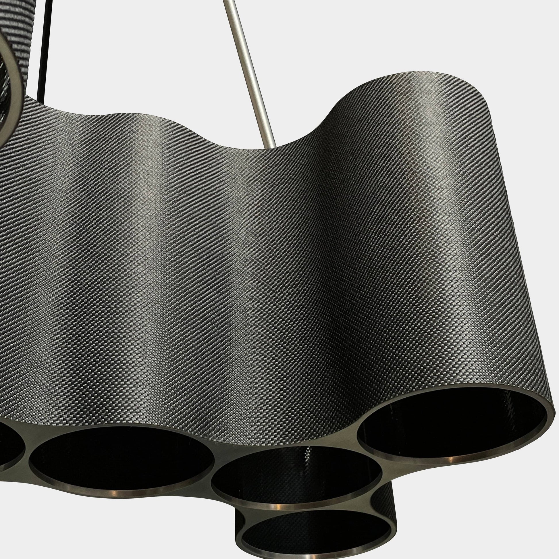 A modern metal chandelier with multiple cylindrical shades connected by thin, curved attachments, hanging from a ceiling mount—a design reminiscent of the Ralph Pucci Linear Cumulus Ceiling Light.