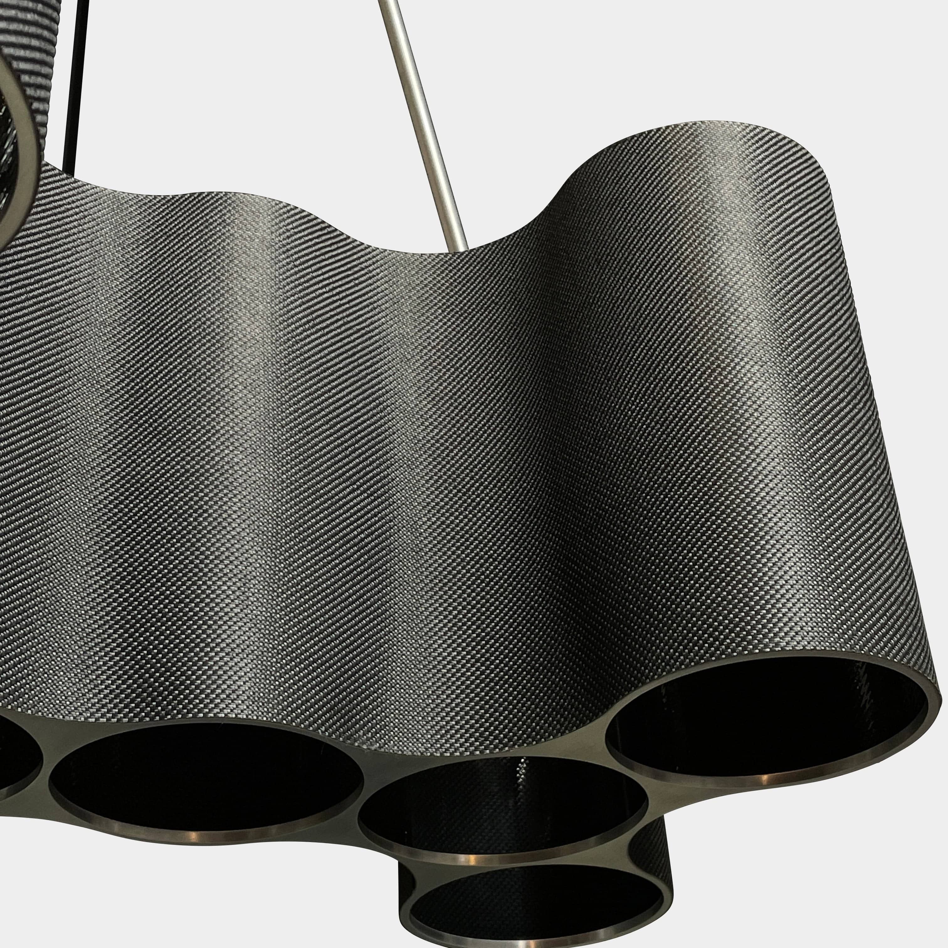 A modern metal chandelier with multiple cylindrical shades connected by thin, curved attachments, hanging from a ceiling mount—a design reminiscent of the Ralph Pucci Linear Cumulus Ceiling Light.