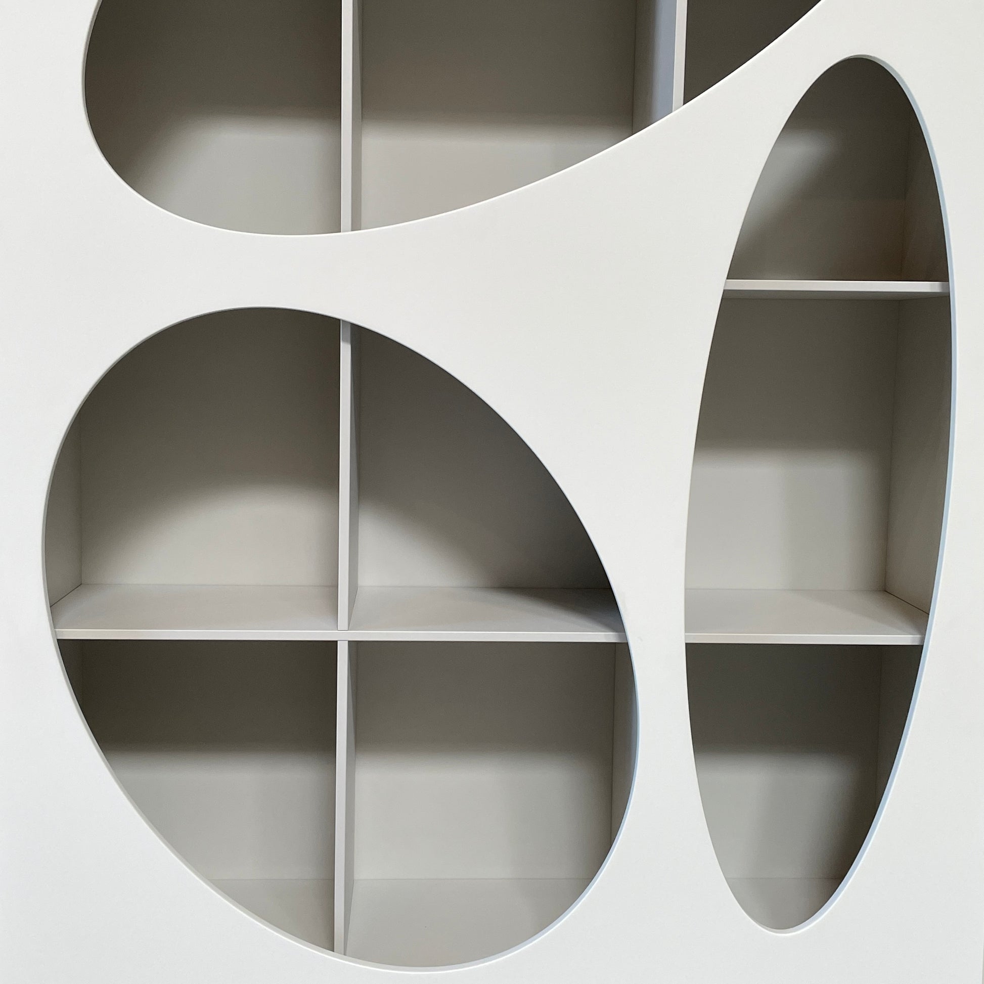 The Roche Bobois Denia Bookcase is a white bookshelf characterized by its abstract design, featuring multiple irregular oval cutouts, nine internal compartments, and integrated LED lighting, reminiscent of ROCHE BOBOIS styling.