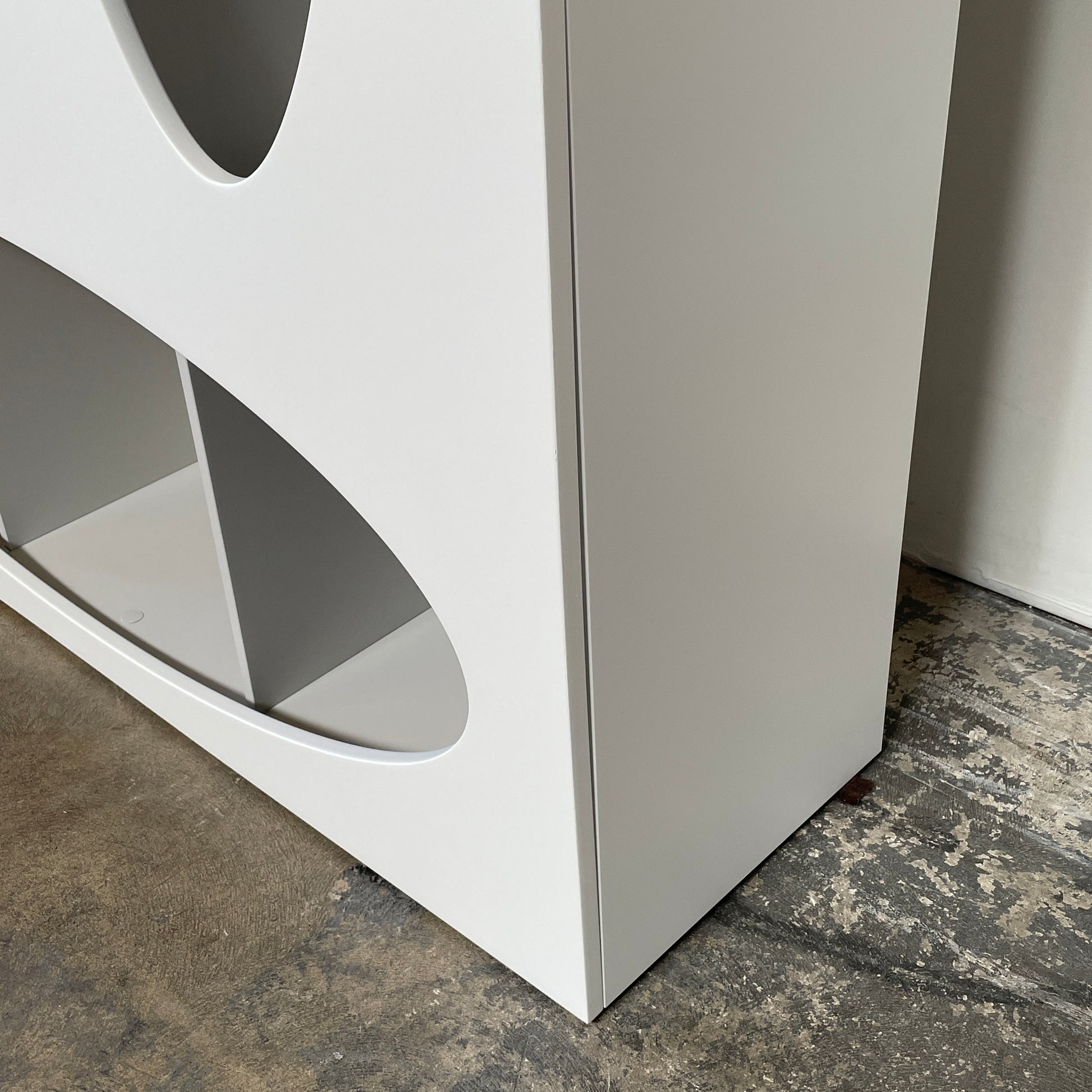 The Roche Bobois Denia Bookcase is a white bookshelf characterized by its abstract design, featuring multiple irregular oval cutouts, nine internal compartments, and integrated LED lighting, reminiscent of ROCHE BOBOIS styling.