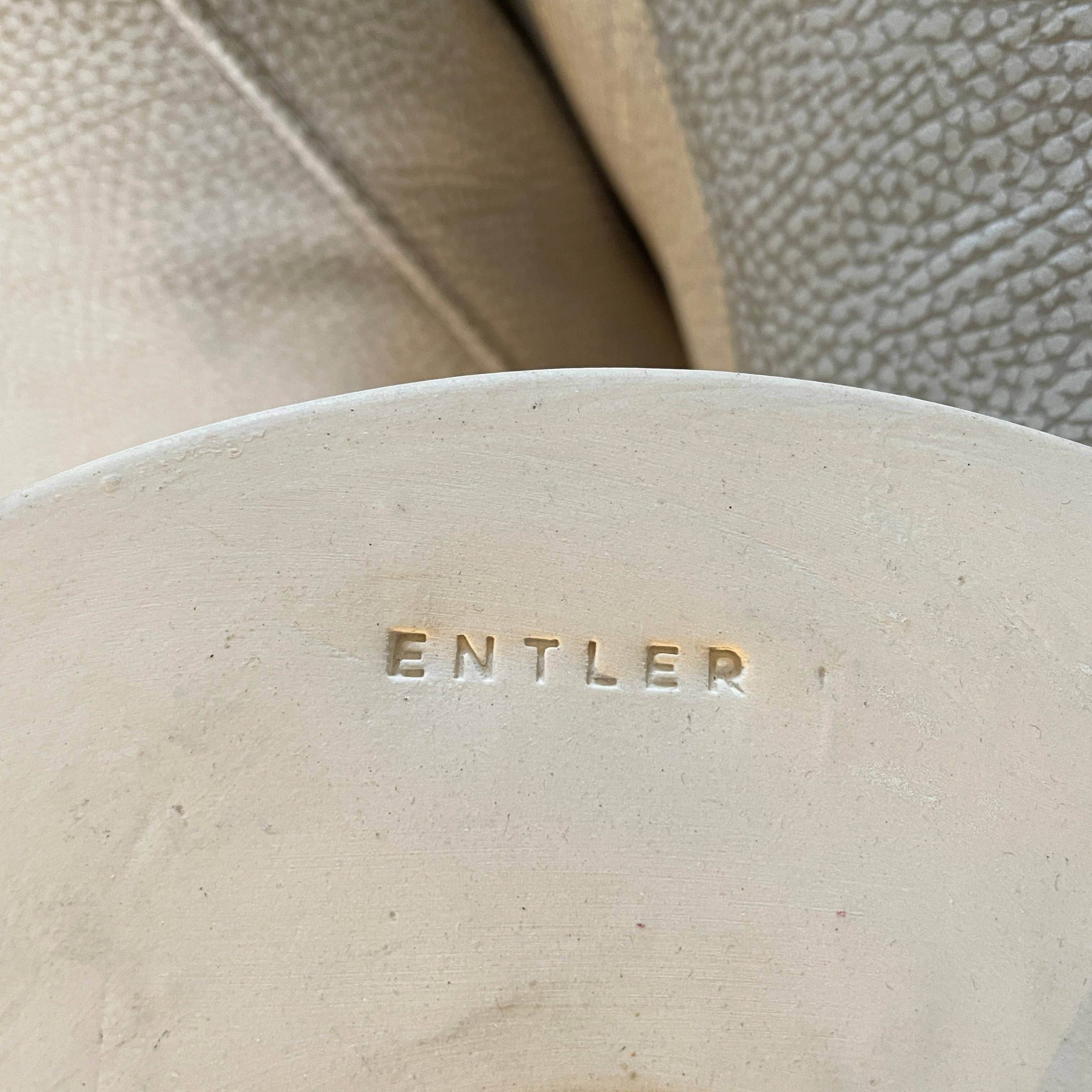 A white, three-legged stand with rounded feet and a flat top against a plain background, reminiscent of the elegant aesthetic found in Entler Studio's 3-Globe Ceiling Light creations.