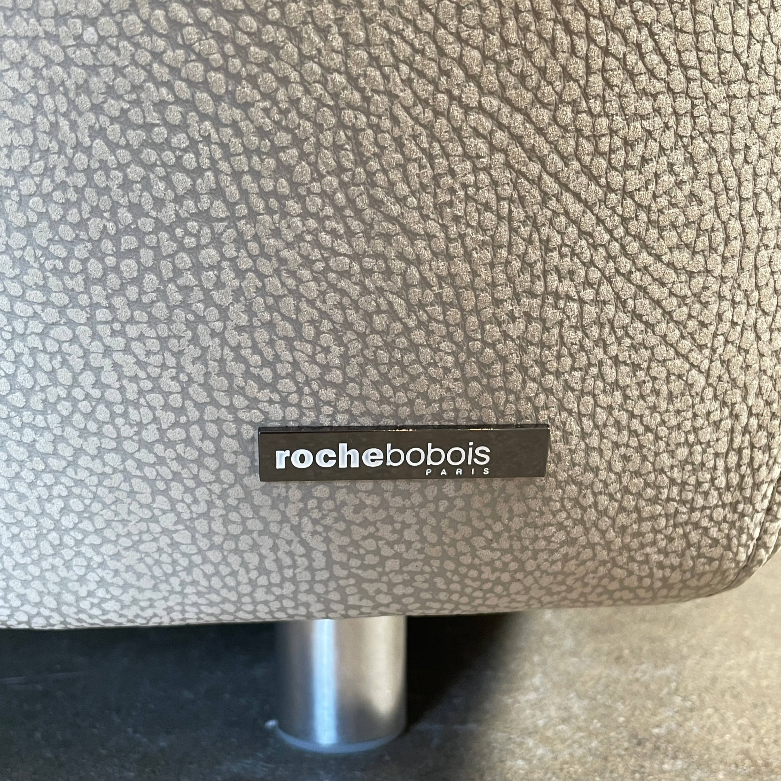 A Roche Bobois Digital Sofa and Ottoman, featuring a curved grey sectional design with three cushions and an additional round ottoman, set against a plain white background.