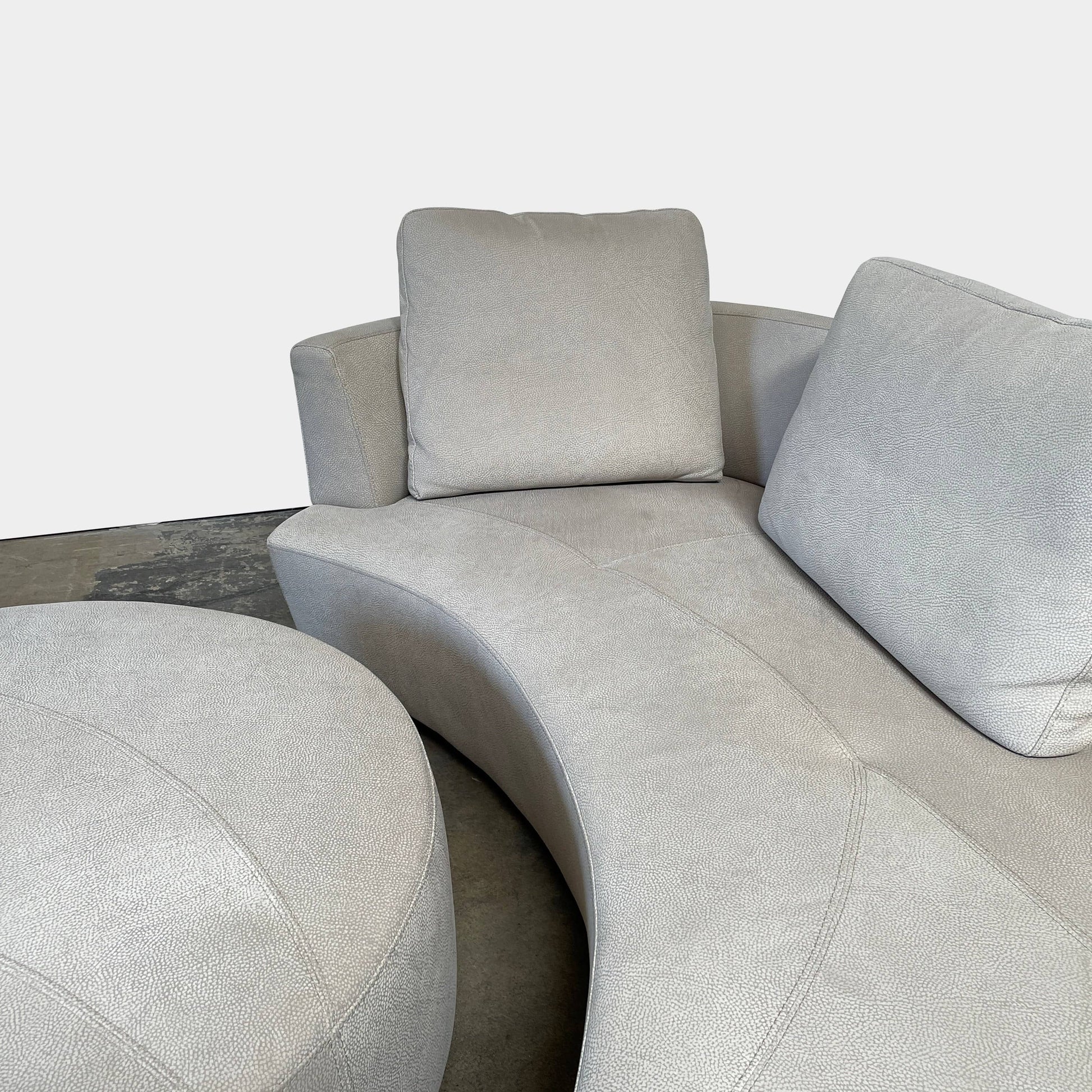 A Roche Bobois Digital Sofa and Ottoman, featuring a curved grey sectional design with three cushions and an additional round ottoman, set against a plain white background.