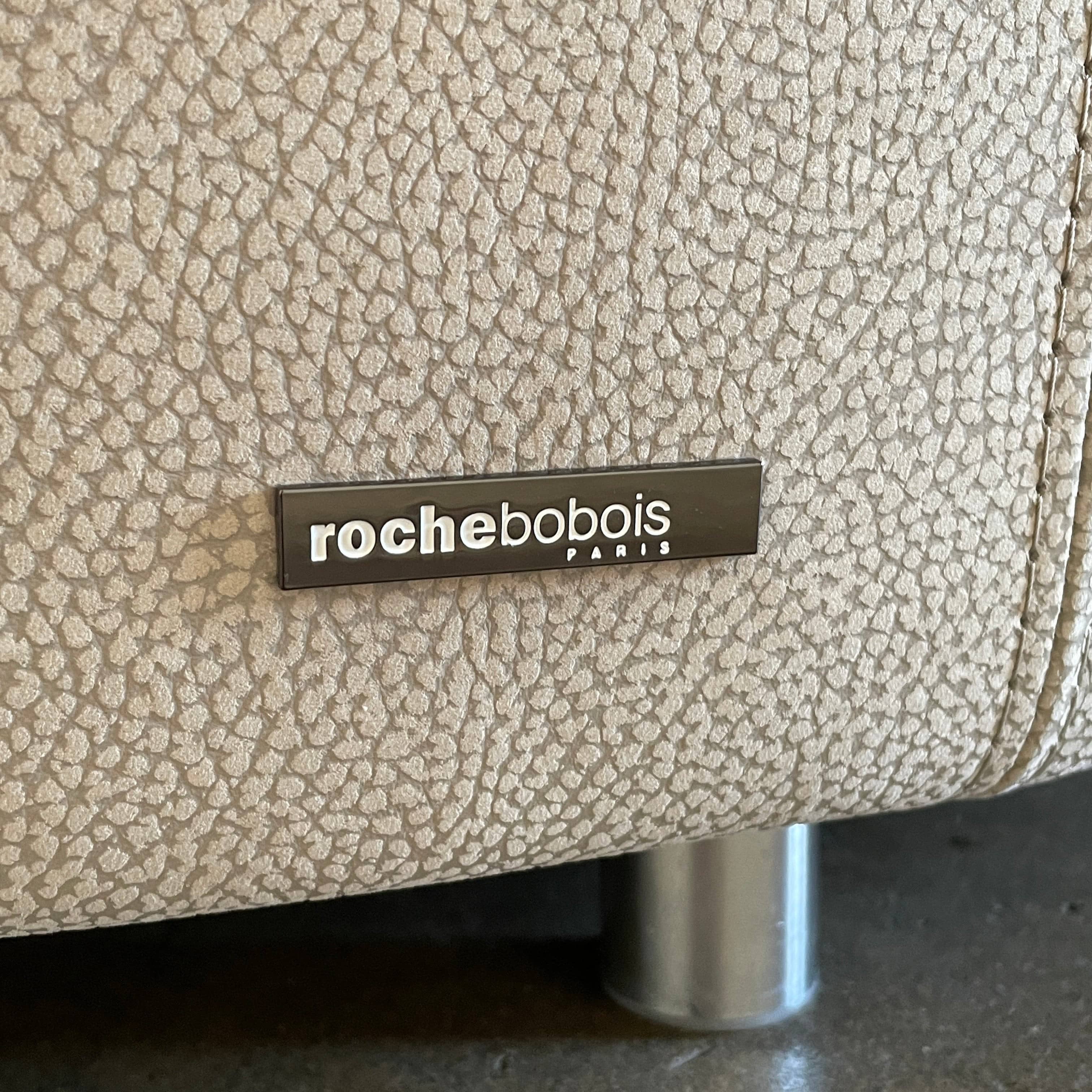 A Roche Bobois Digital Sofa and Ottoman, featuring a curved grey sectional design with three cushions and an additional round ottoman, set against a plain white background.