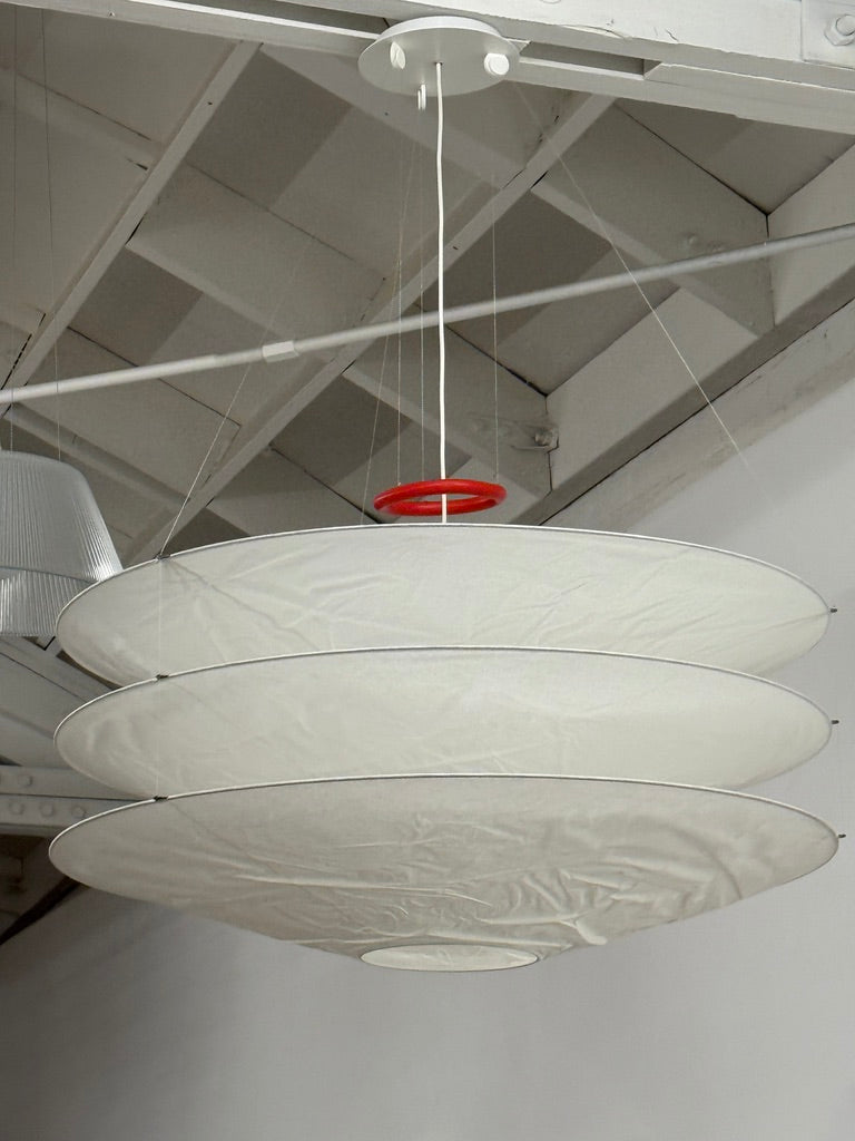 The Ingo Maurer Floatation Suspension Light Medium Size is a modern chandelier with a red ring accent and three overlapping circular discs, showcasing Ingo Maurer's artistry with its elegant and innovative design, suspended elegantly by wires.