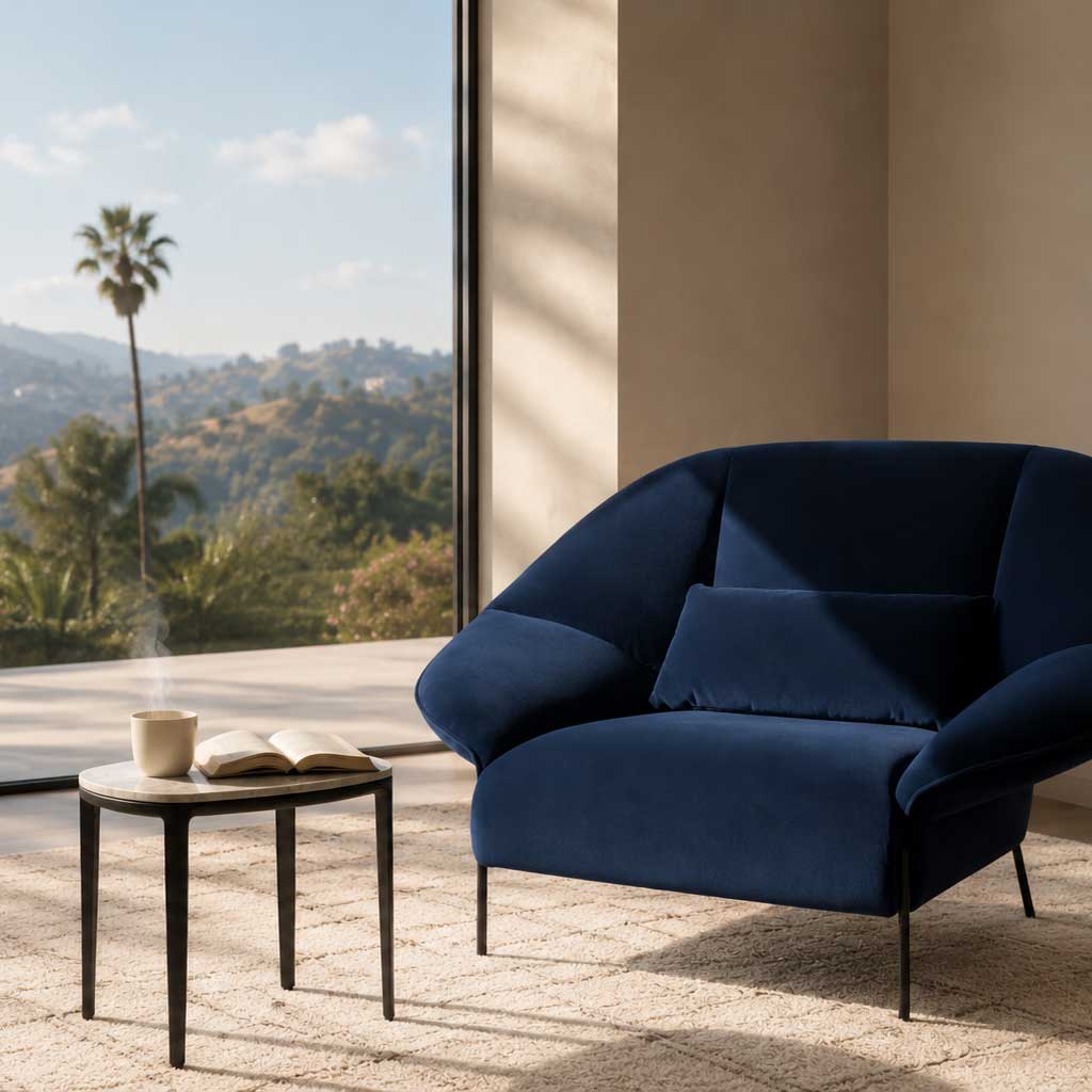 The Ligne Roset Paipai Armchair by Ligne Roset features a navy blue velvet finish, curved cocoon-like seat, matching rectangular cushion, slim black legs, and premium foam construction, displayed against a plain background.