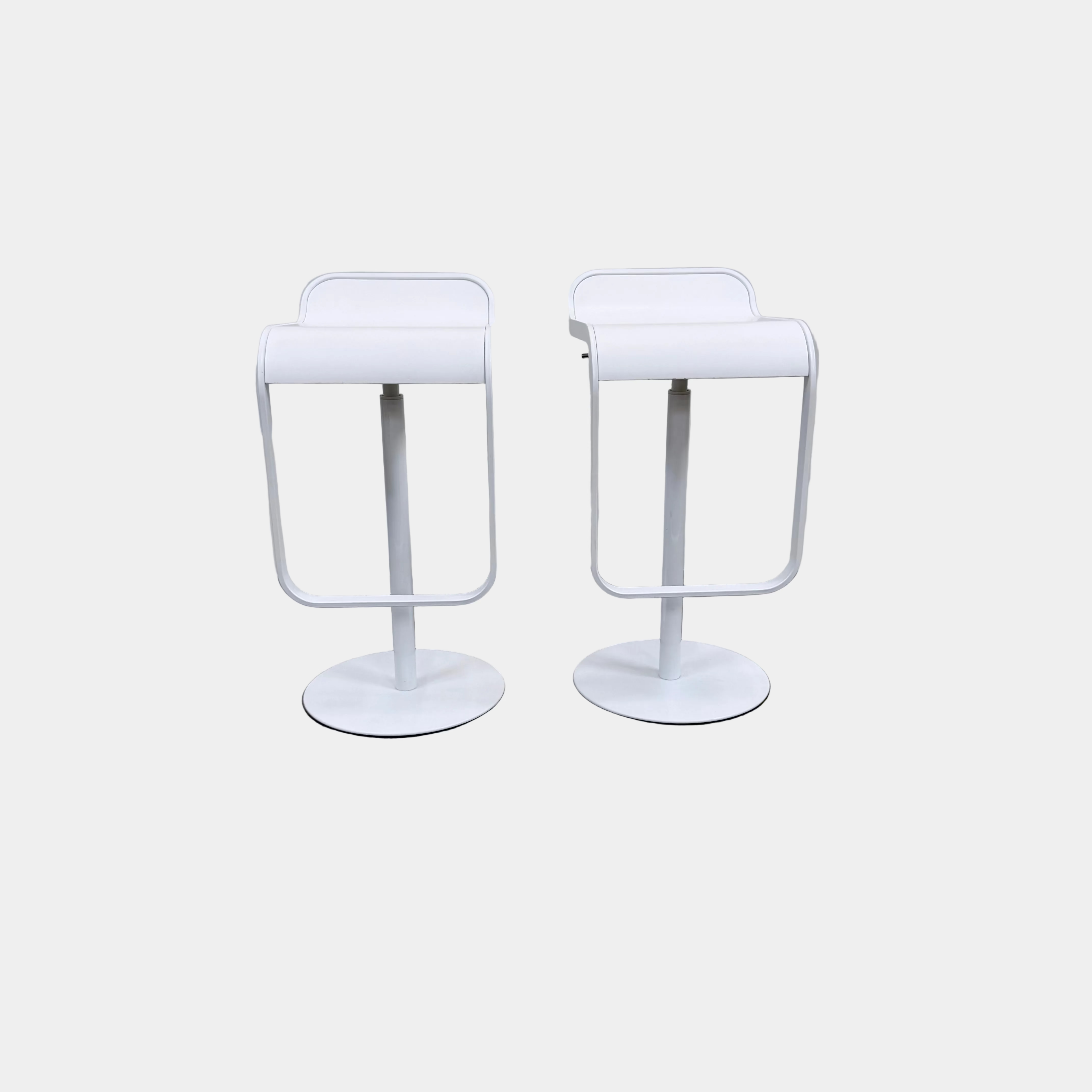 Two white LEM Piston Stools by La Palma featuring pedestal bases and rectangular footrests.