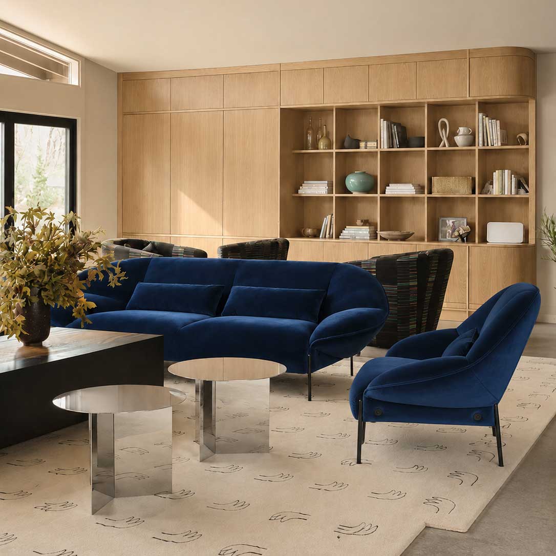 The Ligne Roset Paipaï Sofa by Ligne Roset features deep blue velvet, curved edges, slim black legs, premium foam construction, and two matching rectangular cushions for a cocoon-like seat against a light background.