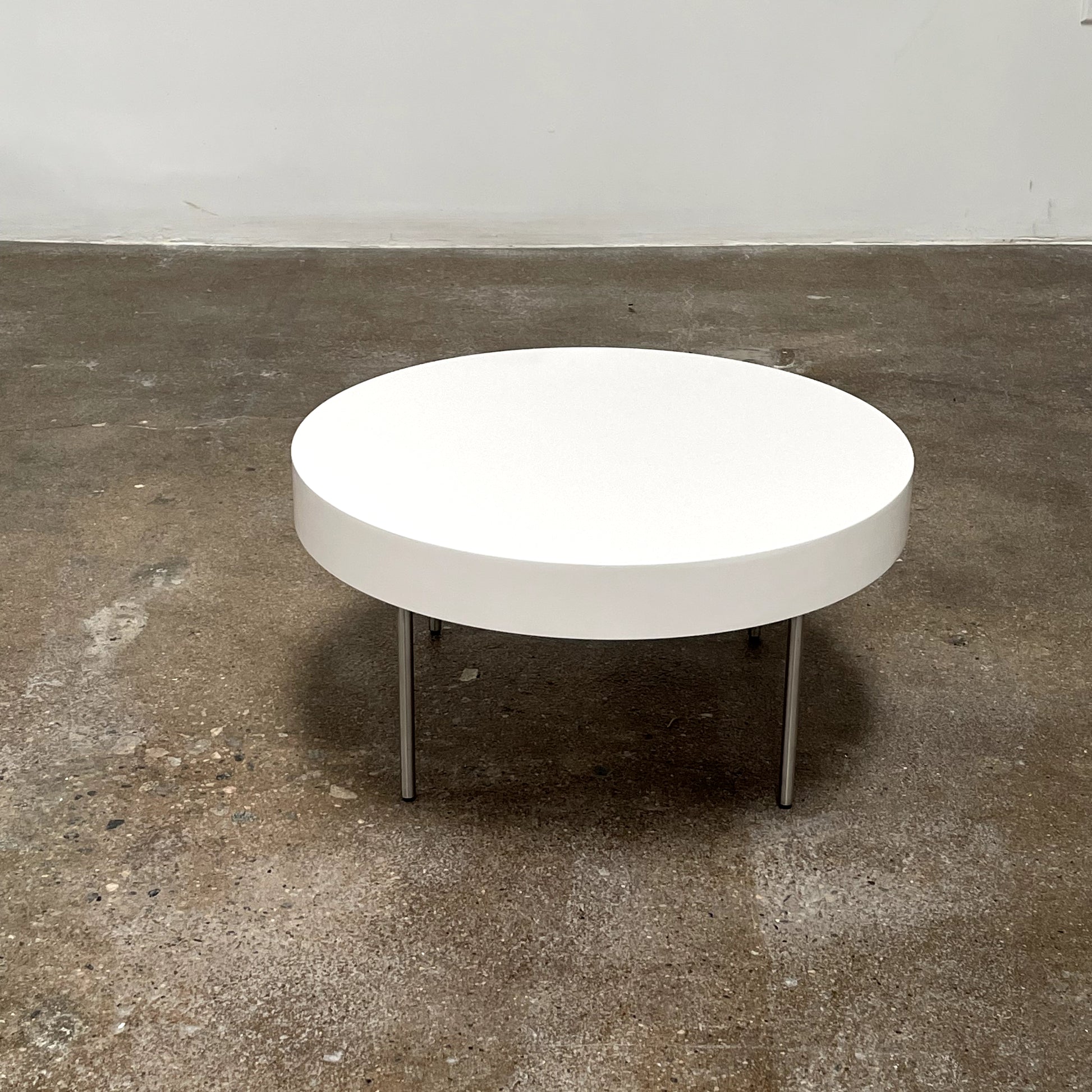 The Ligne Roset White Lacquer Needle Table features a sleek lacquer top and four slender metal legs, perfectly exemplifying modern minimalism against a plain background.