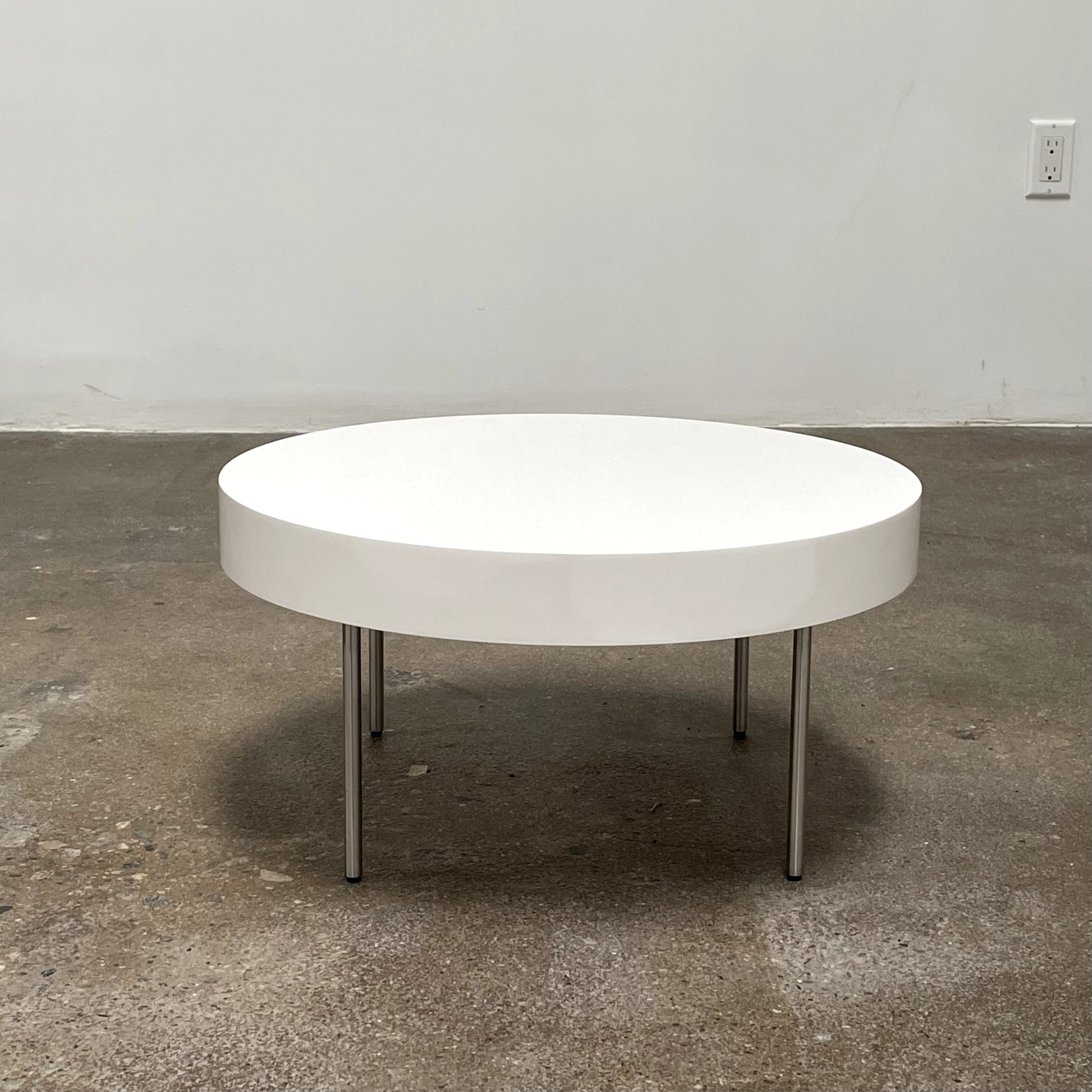 The Ligne Roset White Lacquer Needle Table features a sleek lacquer top and four slender metal legs, perfectly exemplifying modern minimalism against a plain background.