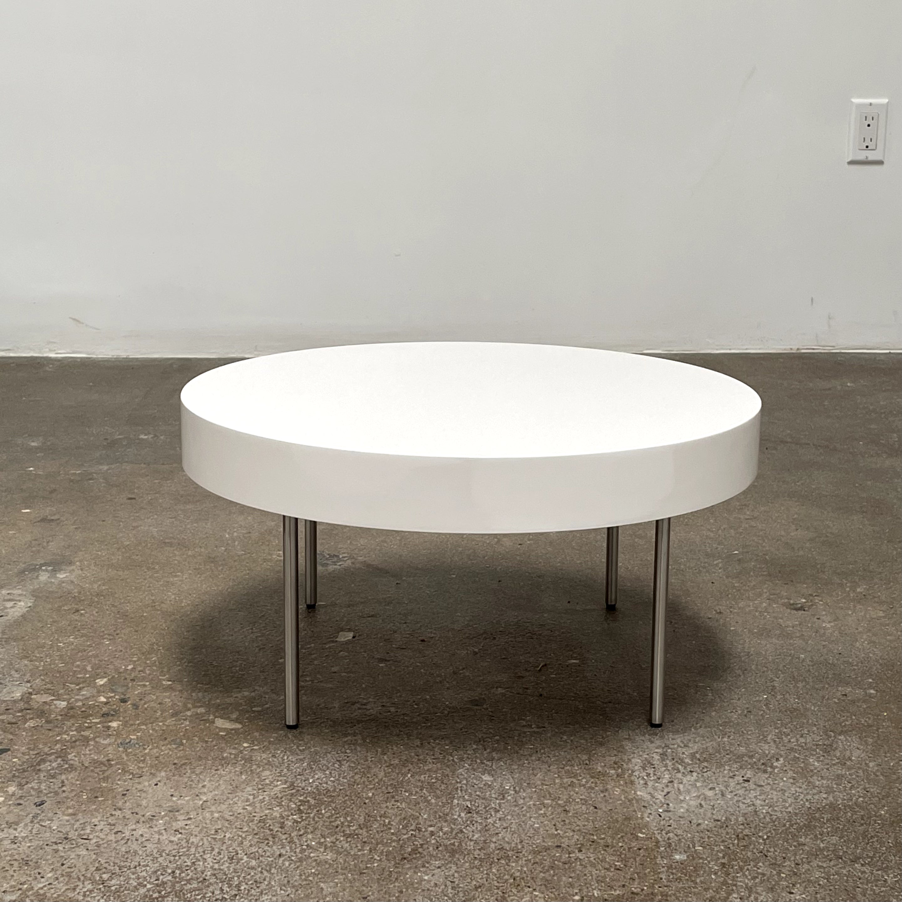 The Ligne Roset White Lacquer Needle Table features a sleek lacquer top and four slender metal legs, perfectly exemplifying modern minimalism against a plain background.