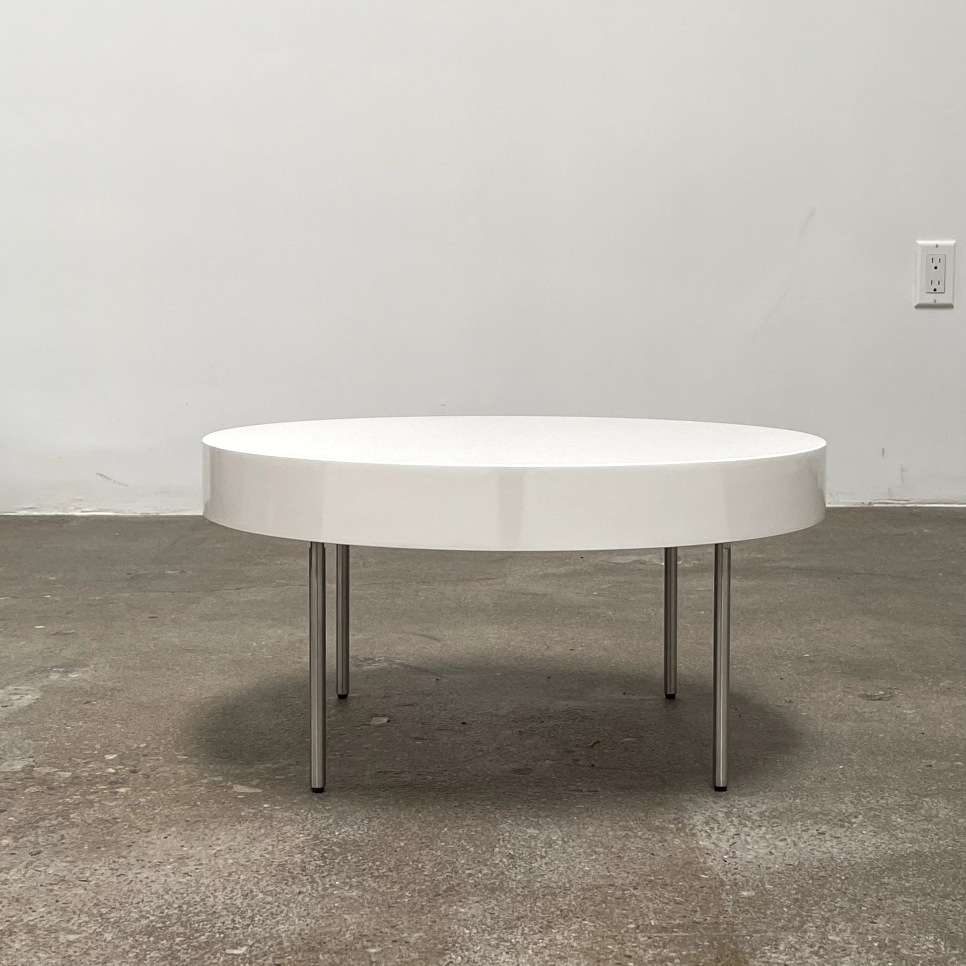 The Ligne Roset White Lacquer Needle Table features a sleek lacquer top and four slender metal legs, perfectly exemplifying modern minimalism against a plain background.