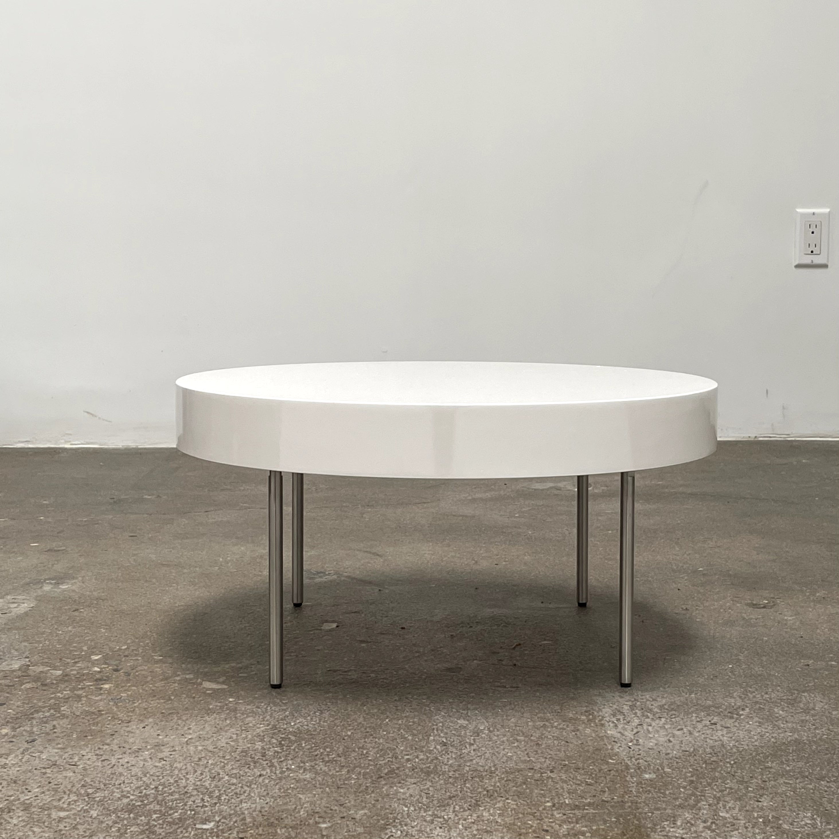 The Ligne Roset White Lacquer Needle Table features a sleek lacquer top and four slender metal legs, perfectly exemplifying modern minimalism against a plain background.