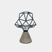 The Magis Grey Swivel Chair One With Concrete Base, designed by Konstantin Grcic, showcases a geometric open lattice design on a concrete base, sitting gracefully on a textured floor against a plain wall.