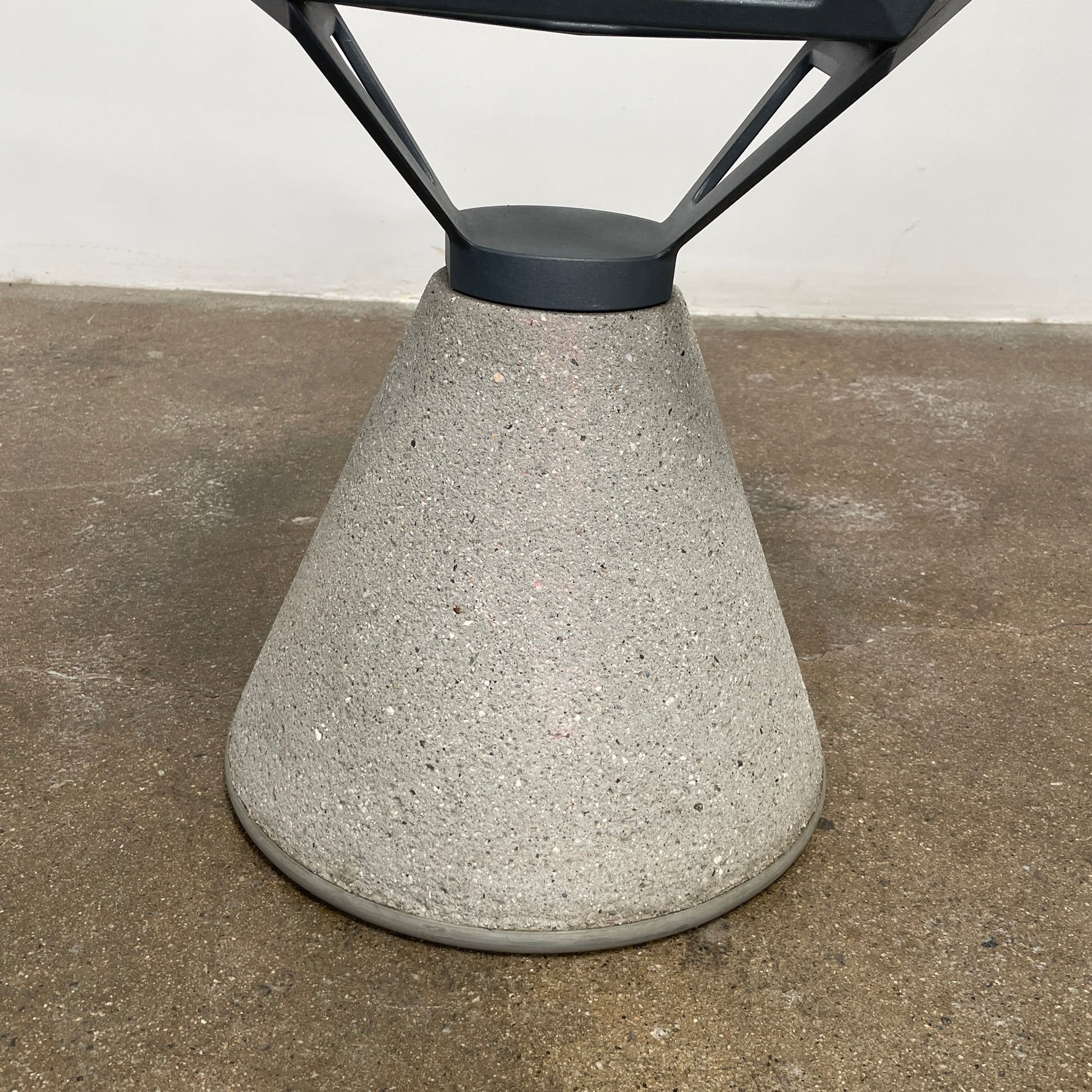 The Magis Grey Swivel Chair One With Concrete Base, designed by Konstantin Grcic, showcases a geometric open lattice design on a concrete base, sitting gracefully on a textured floor against a plain wall.