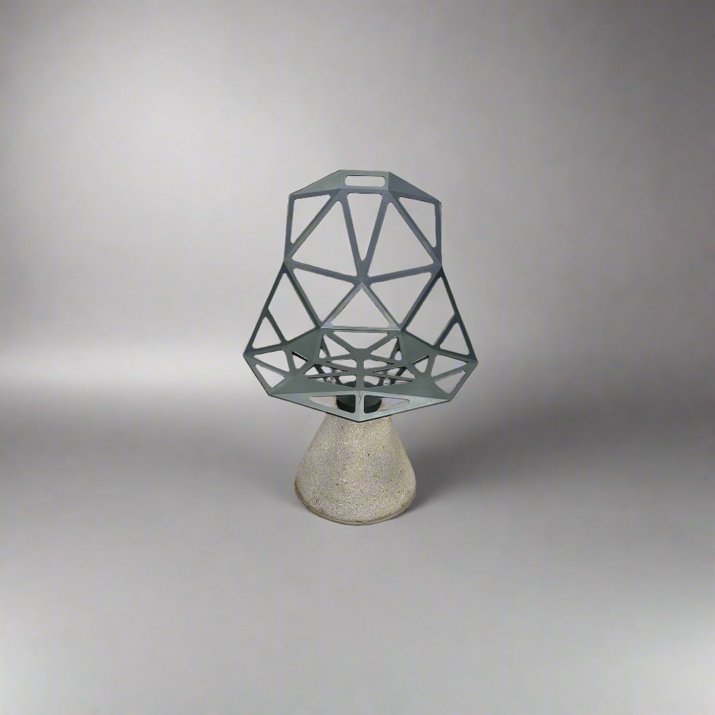 The Magis Grey Swivel Chair One With Concrete Base, designed by Konstantin Grcic, showcases a geometric open lattice design on a concrete base, sitting gracefully on a textured floor against a plain wall.