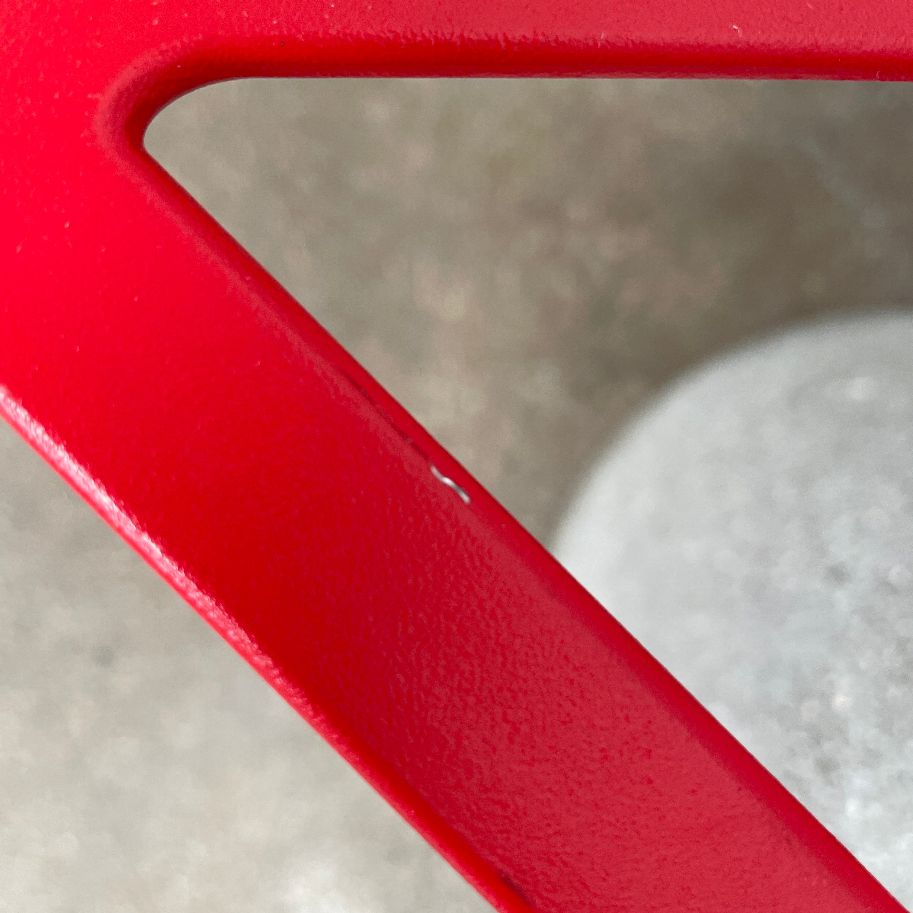 A Magis Red Chair One with a swivel base is positioned on a concrete foundation against a plain white background, reflecting the innovative style of Konstantin Grcic's designs.