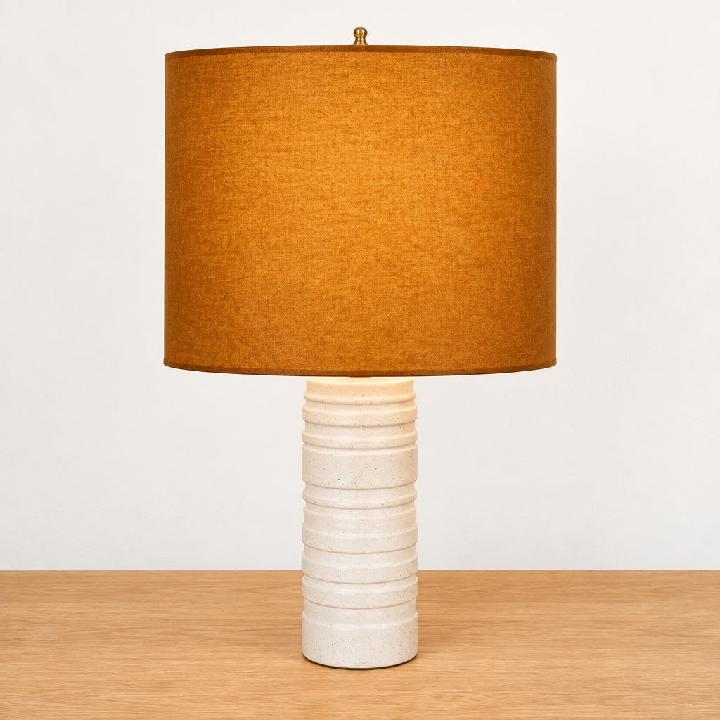Two Shelter Brasilia Lamp with textured white bases and orange cylindrical shades are displayed on a beige stone surface against a gray background.