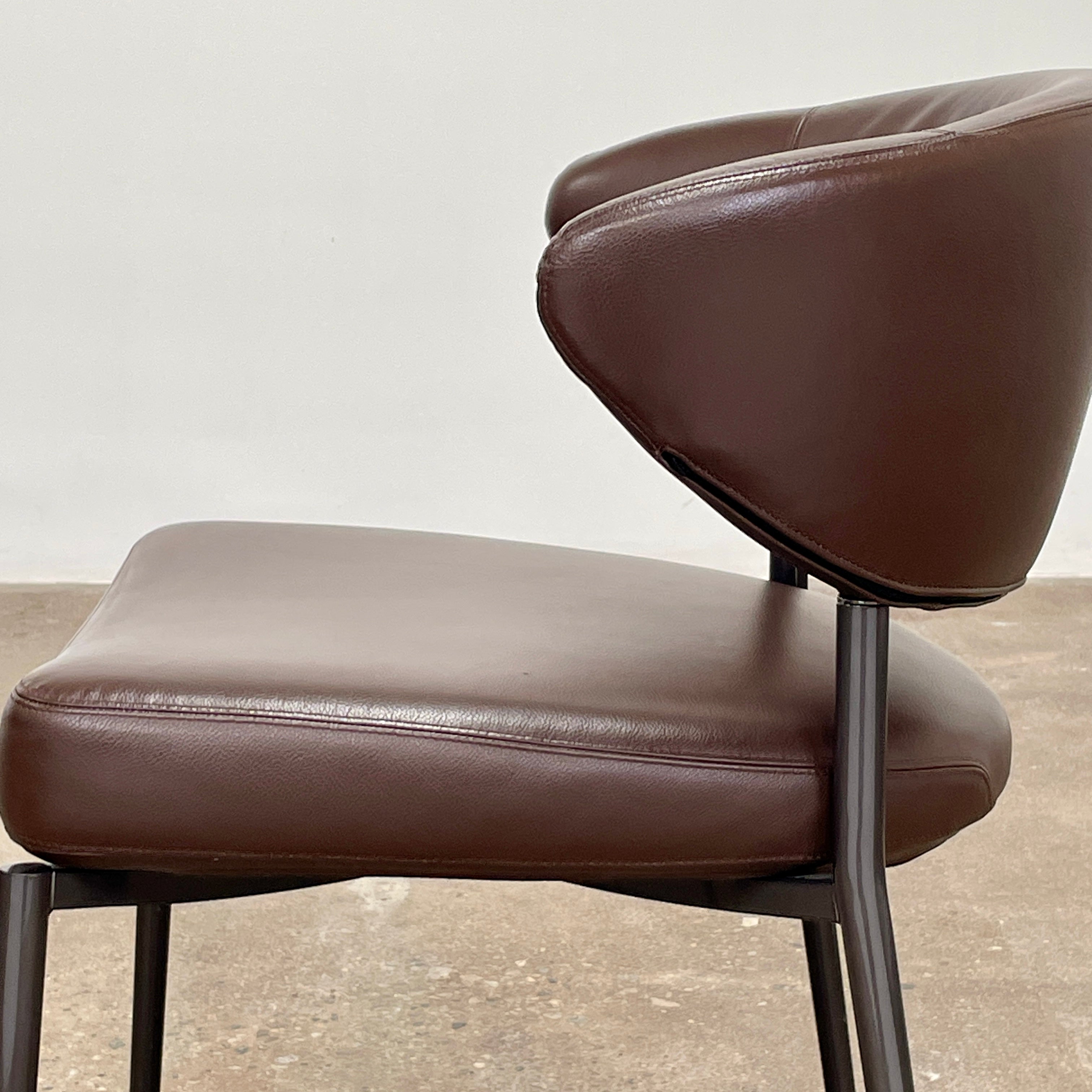 A set of six Minotti Mills Dining Chairs, featuring Scandinavian design with brown leather upholstery and black metal legs, is arranged in a staggered formation against a plain background.