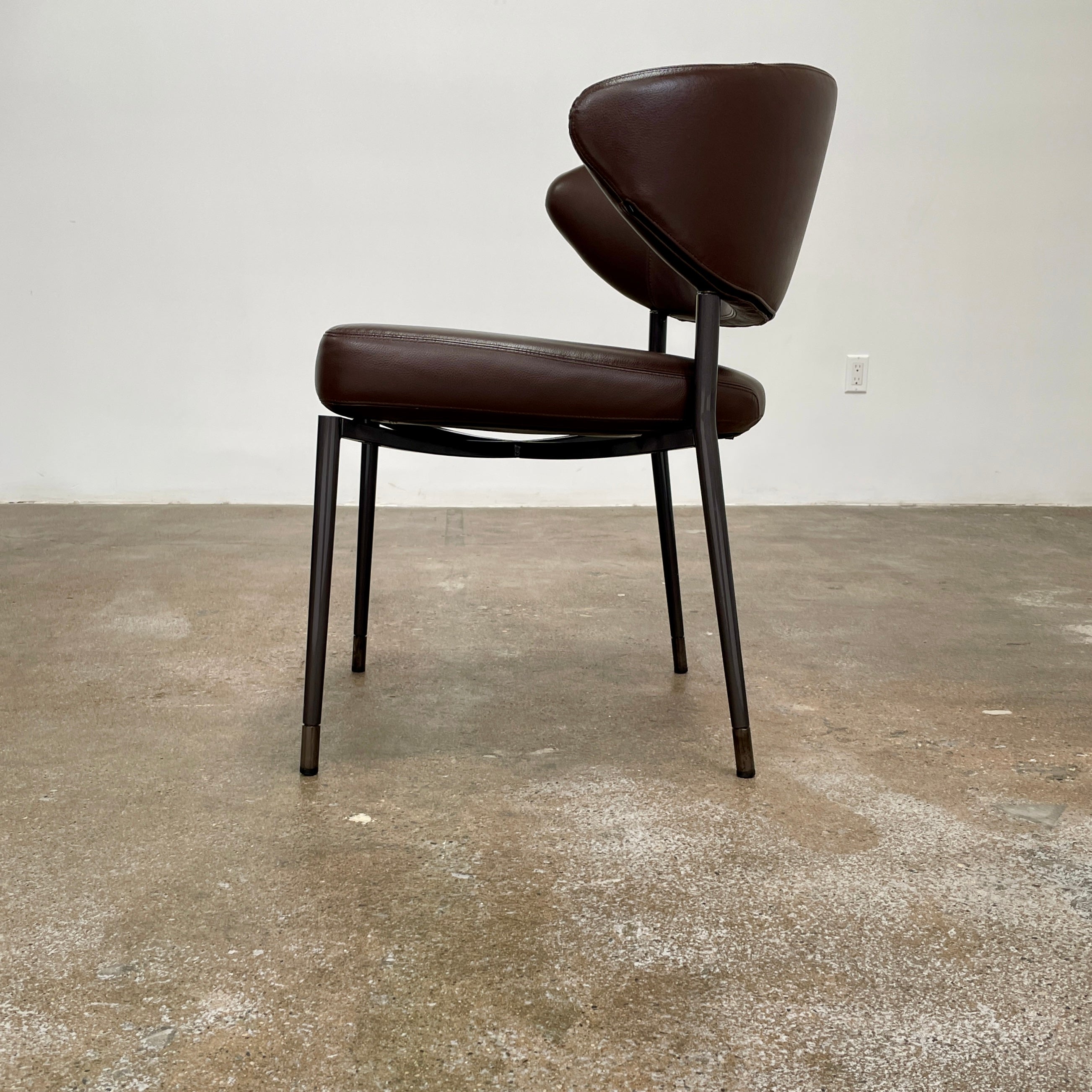A set of six Minotti Mills Dining Chairs, featuring Scandinavian design with brown leather upholstery and black metal legs, is arranged in a staggered formation against a plain background.