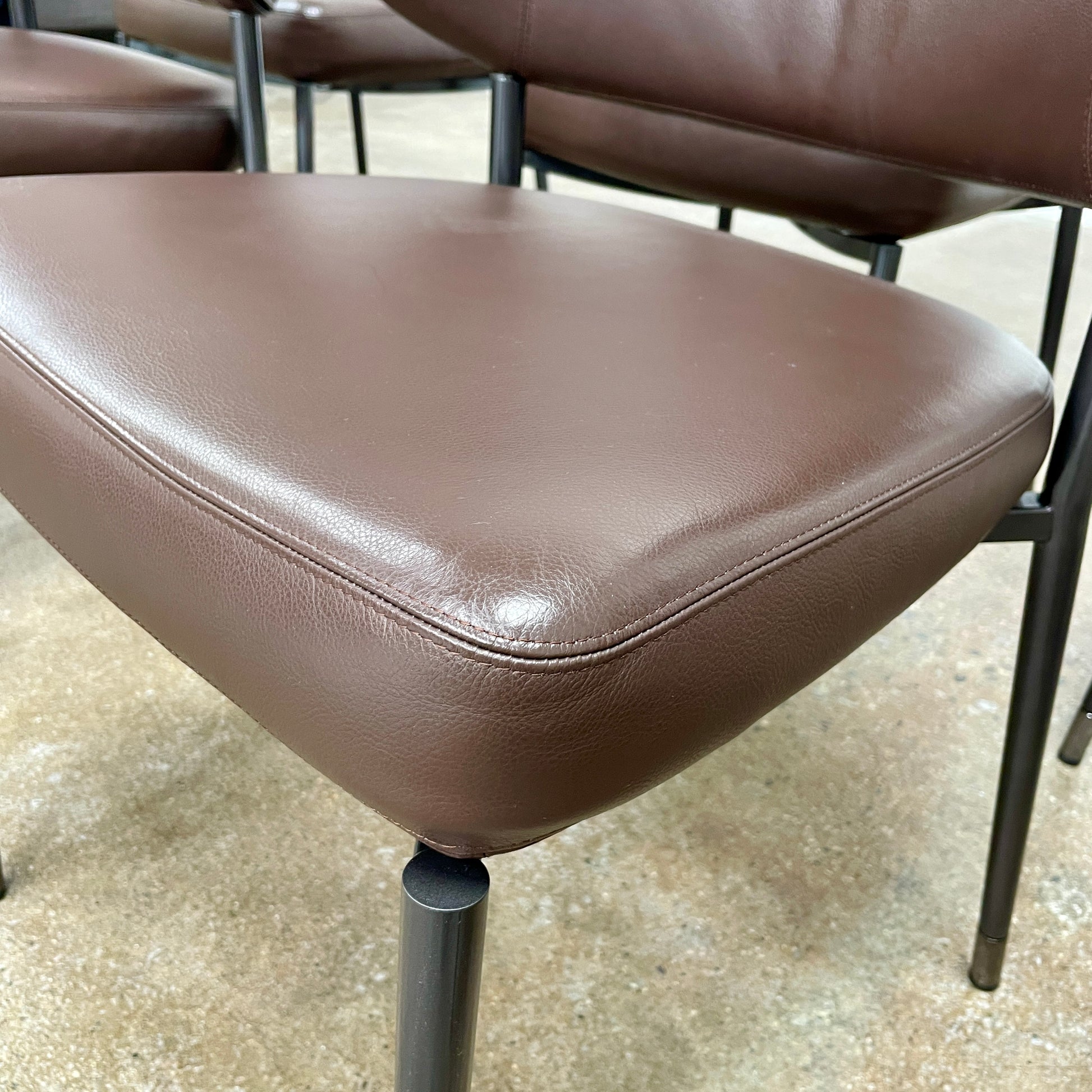 A set of six Minotti Mills Dining Chairs, featuring Scandinavian design with brown leather upholstery and black metal legs, is arranged in a staggered formation against a plain background.