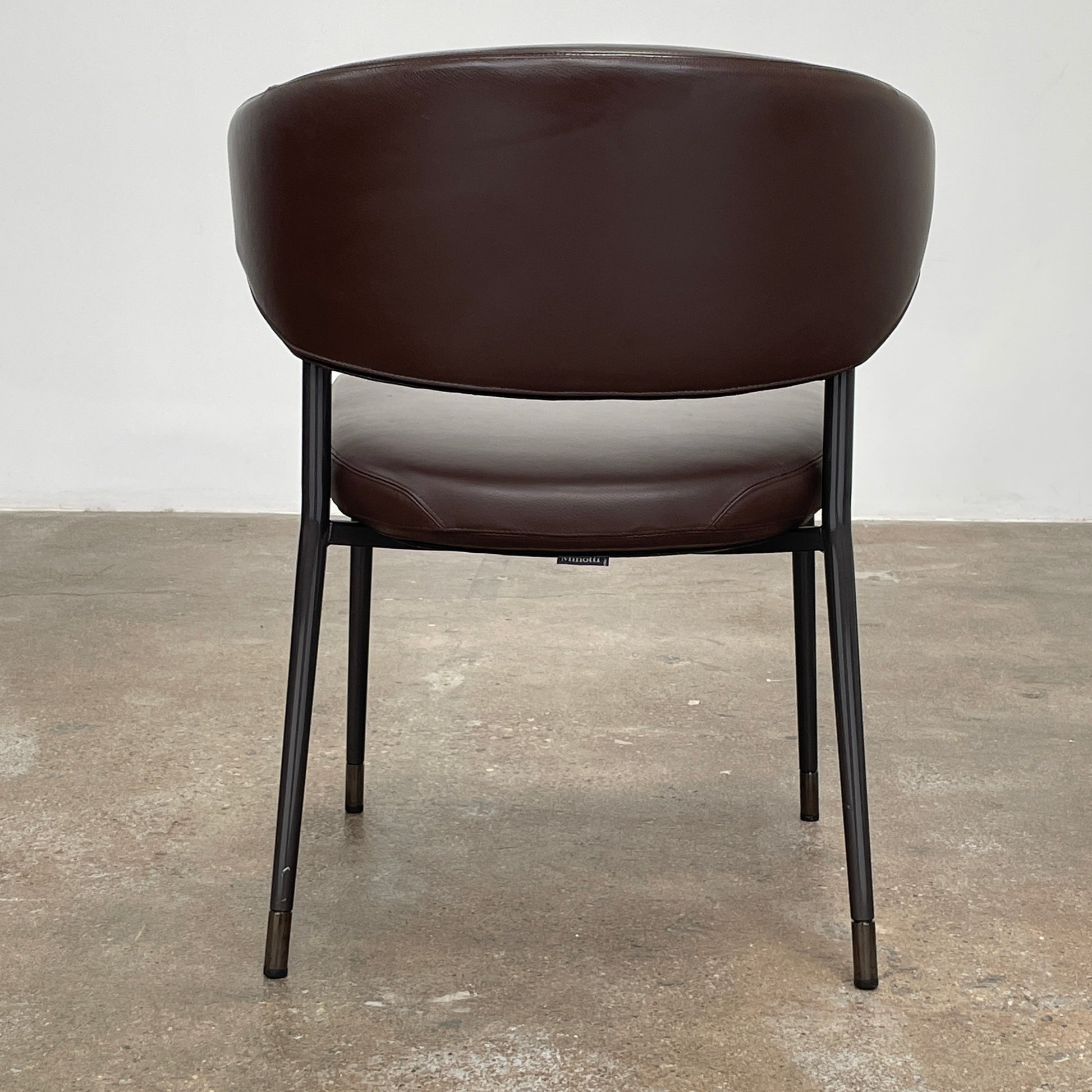 A set of six Minotti Mills Dining Chairs, featuring Scandinavian design with brown leather upholstery and black metal legs, is arranged in a staggered formation against a plain background.