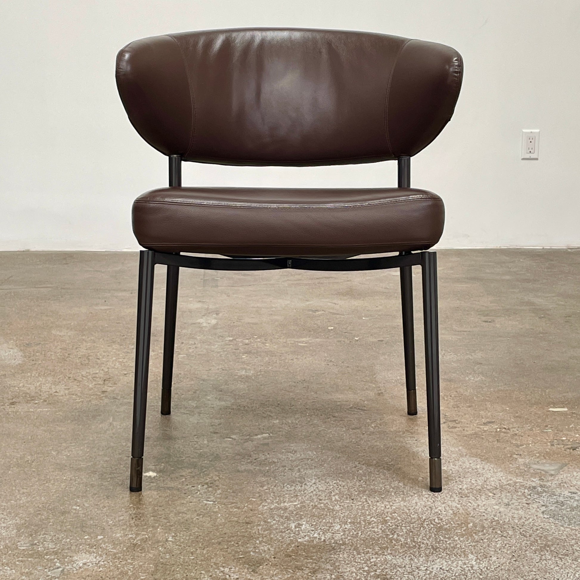 A set of six Minotti Mills Dining Chairs, featuring Scandinavian design with brown leather upholstery and black metal legs, is arranged in a staggered formation against a plain background.