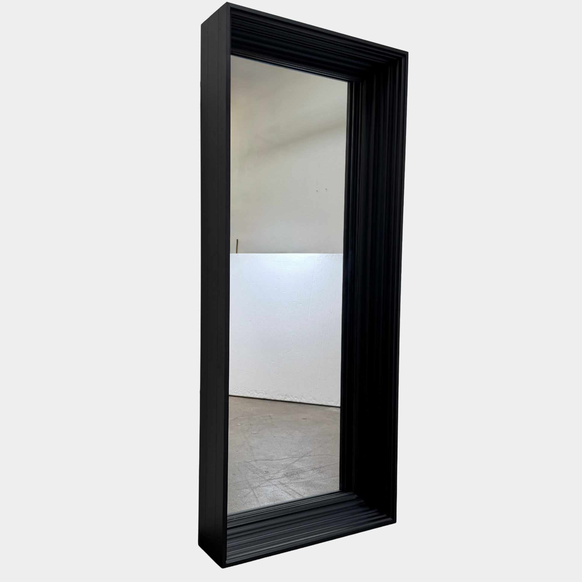 A person kneels in front of the Moooi Frame Mirror by Moooi—a large, rectangular mirror with a sleek black aluminum frame—while taking a photo. The mirror reflects furniture and industrial shelving within a well-lit room.