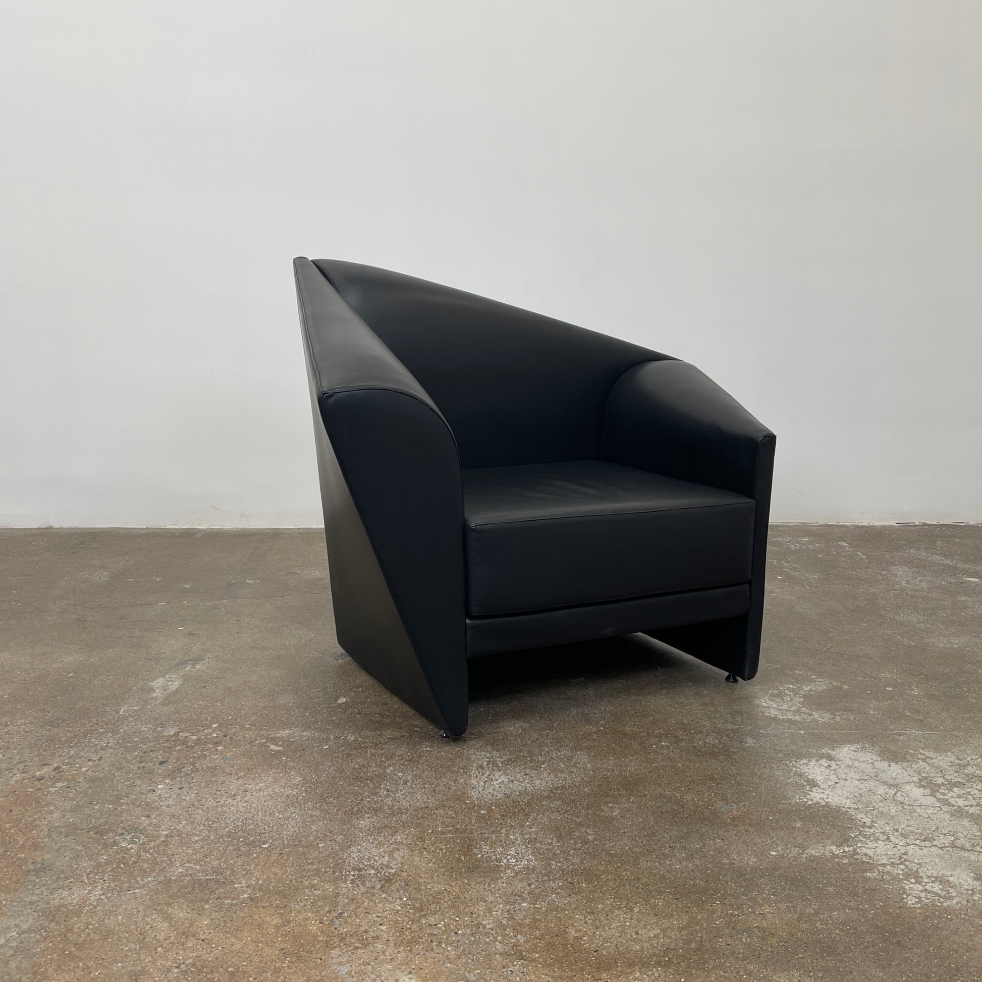 The Lilly of the Wind Armchair by Paolo Pallucco and Mireille Rivier for Pallucco Italia showcases a black leather finish and angular, modern design on a light gray background, echoing Paolo Pallucco's post-modern style.