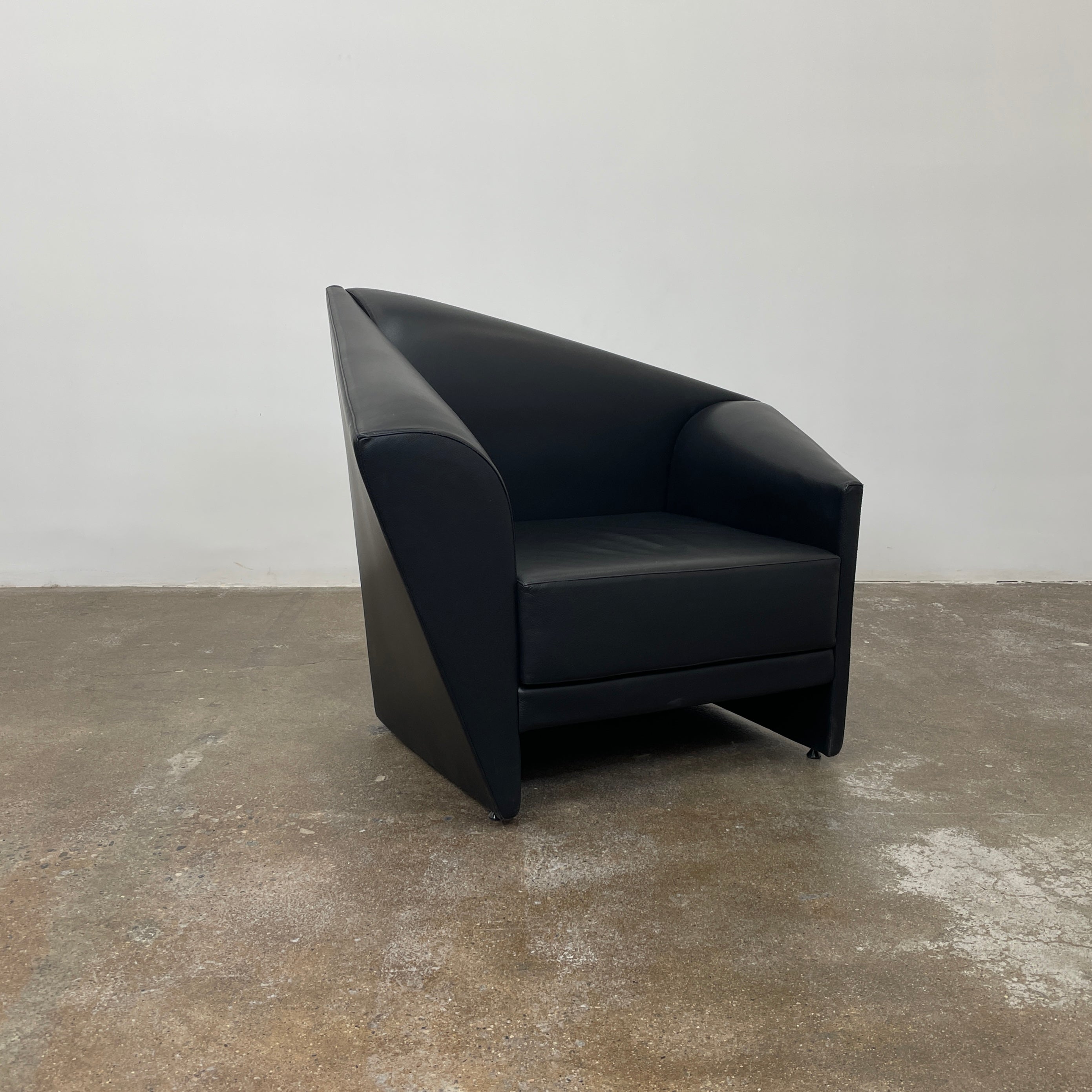 The Lilly of the Wind Armchair by Paolo Pallucco and Mireille Rivier for Pallucco Italia showcases a black leather finish and angular, modern design on a light gray background, echoing Paolo Pallucco's post-modern style.