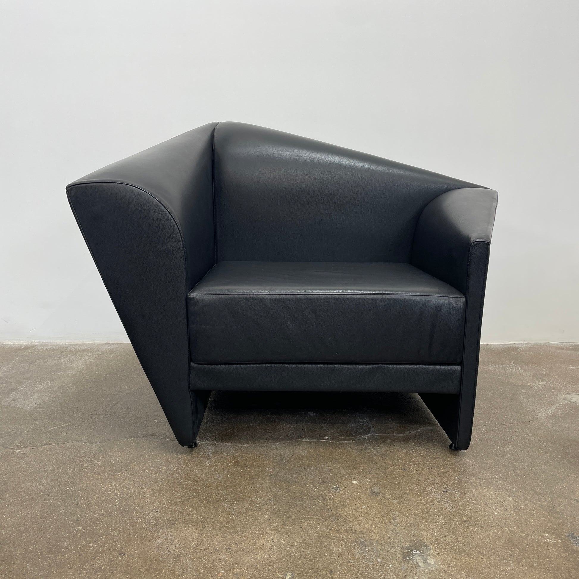 The Lilly of the Wind Armchair by Paolo Pallucco and Mireille Rivier for Pallucco Italia showcases a black leather finish and angular, modern design on a light gray background, echoing Paolo Pallucco's post-modern style.