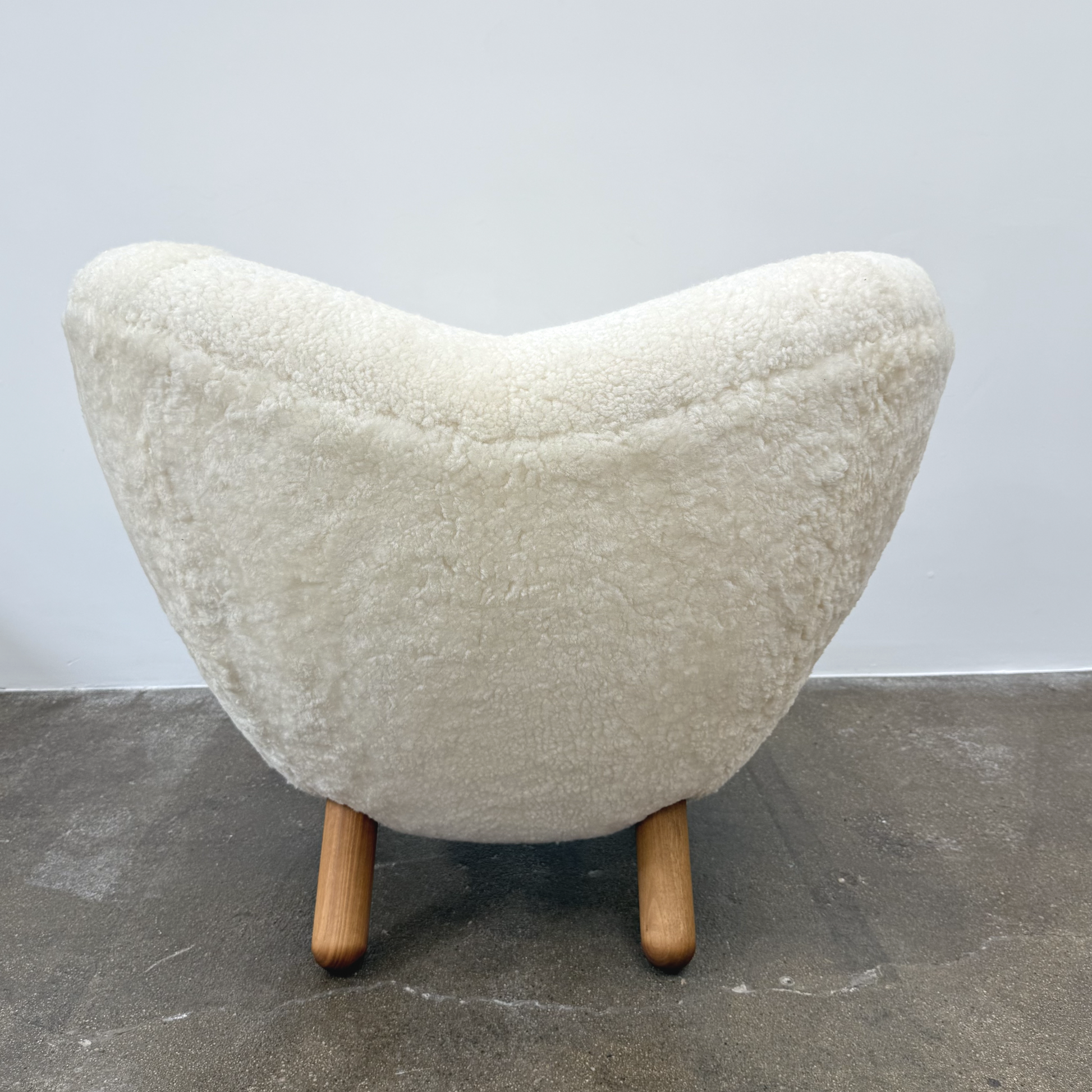 The House of Finn Juhl Finn Juhl Pelican Chair Sheepskin, with curved armrests and wooden legs, is displayed against a plain white background.