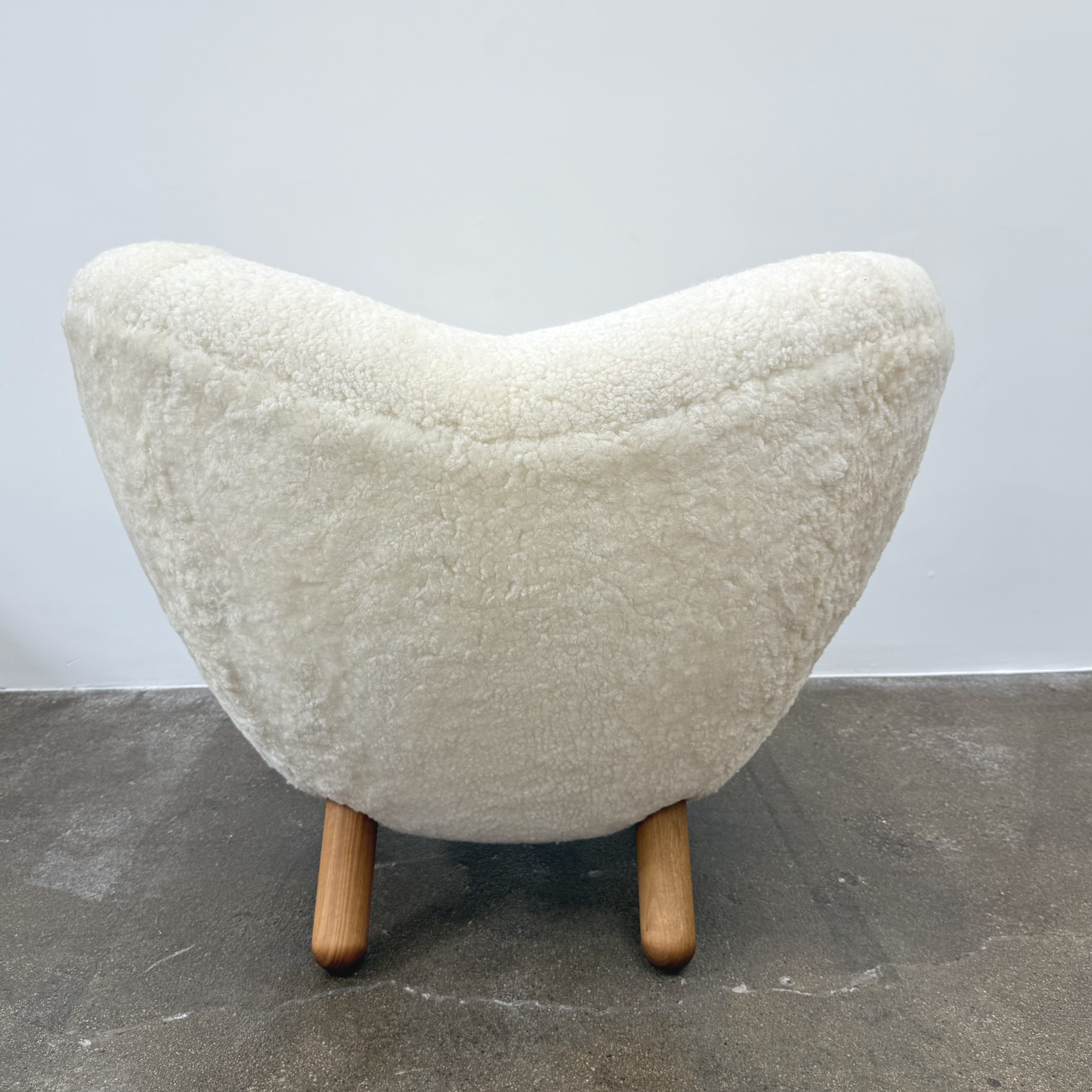 The House of Finn Juhl Finn Juhl Pelican Chair Sheepskin, with curved armrests and wooden legs, is displayed against a plain white background.