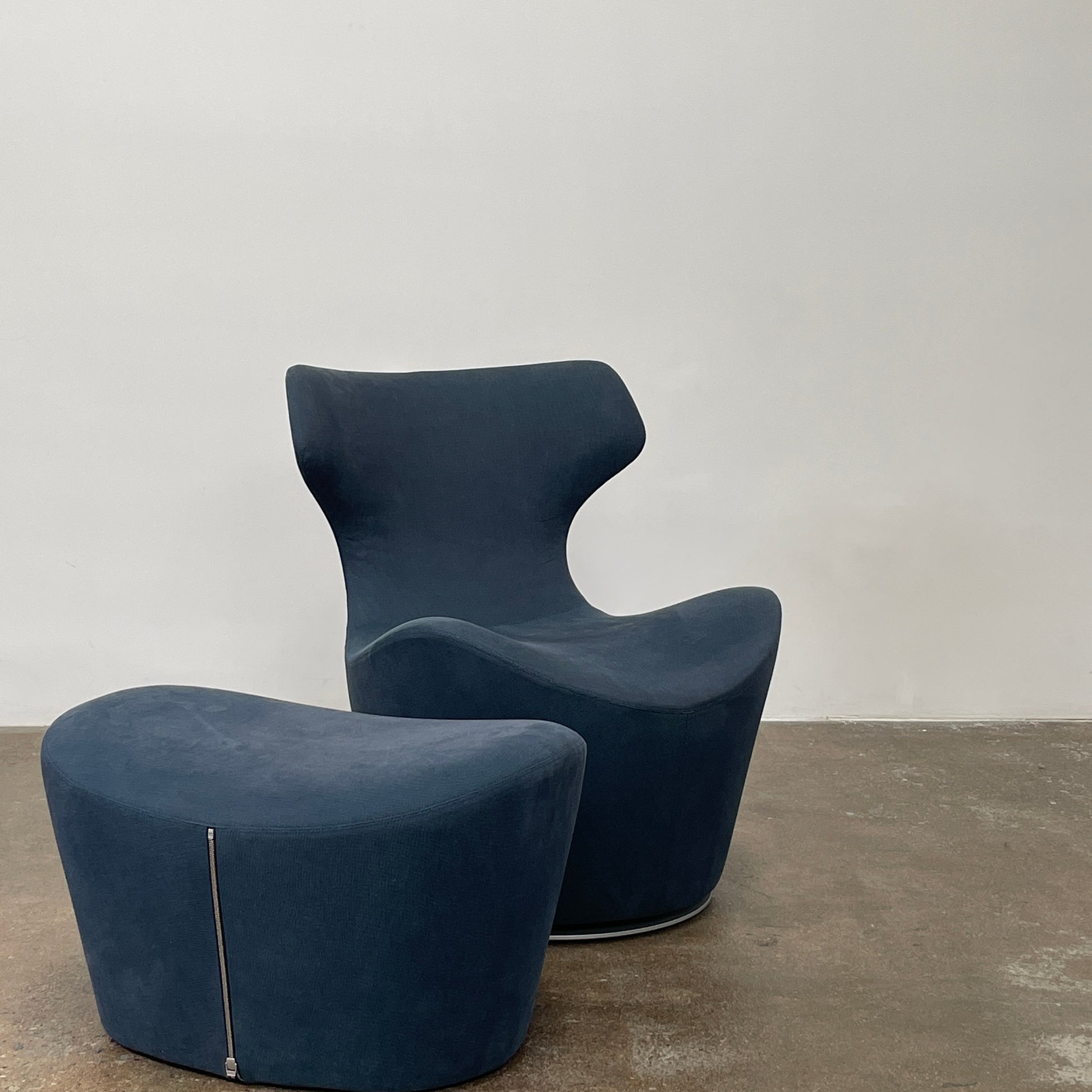 The B&B Italia Piccola Papilio Swivel Armchair is a modern piece with an abstract form and high curved backrest. Made from teal fabric, it stands on a swivel base against a plain white background.