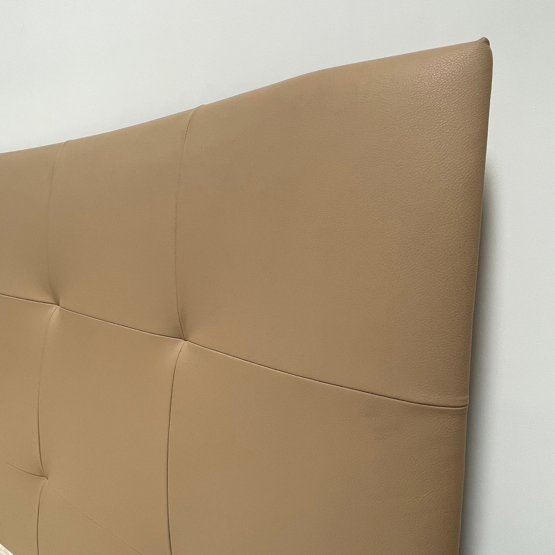 The Poltrona Frau Aurora Due King Bed, crafted by designer Tito Agnoli, boasts a minimalist and modern style with its beige tufted headboard set against a plain light gray wall.