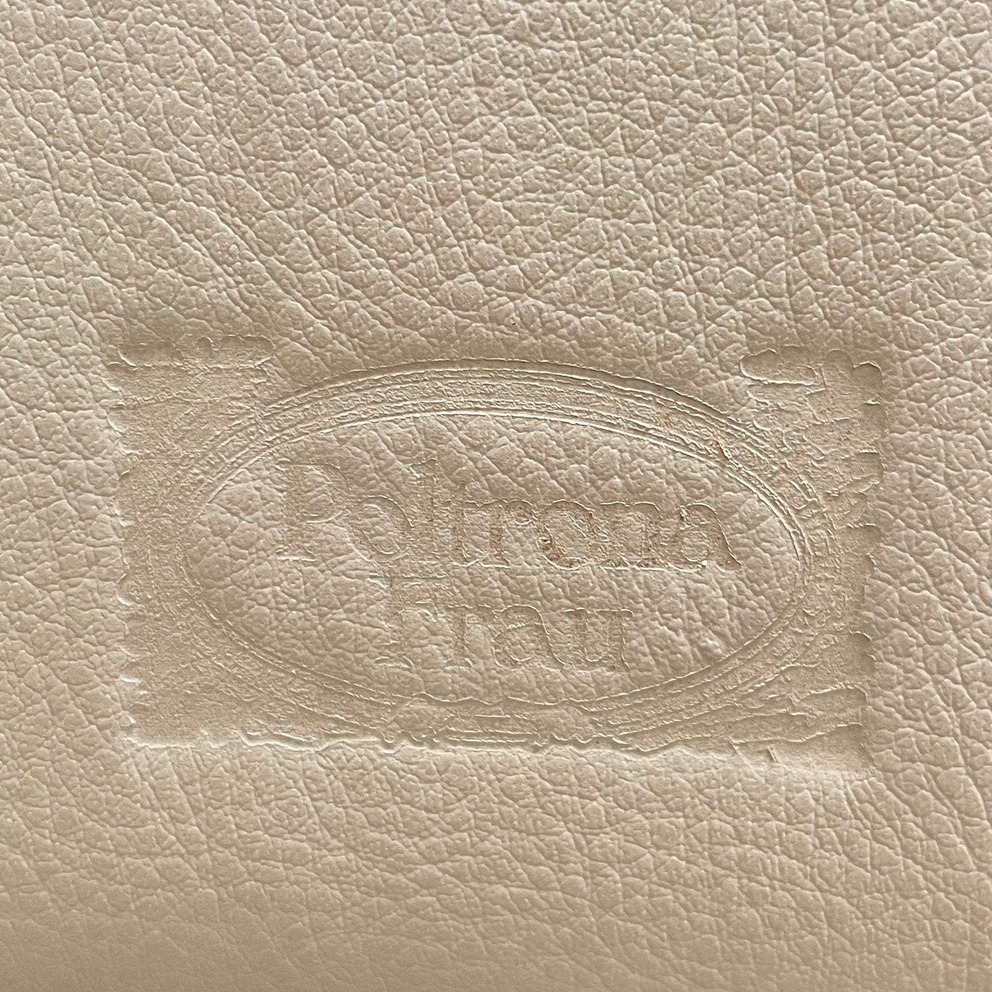 The Poltrona Frau Aurora Due King Bed, crafted by designer Tito Agnoli, boasts a minimalist and modern style with its beige tufted headboard set against a plain light gray wall.