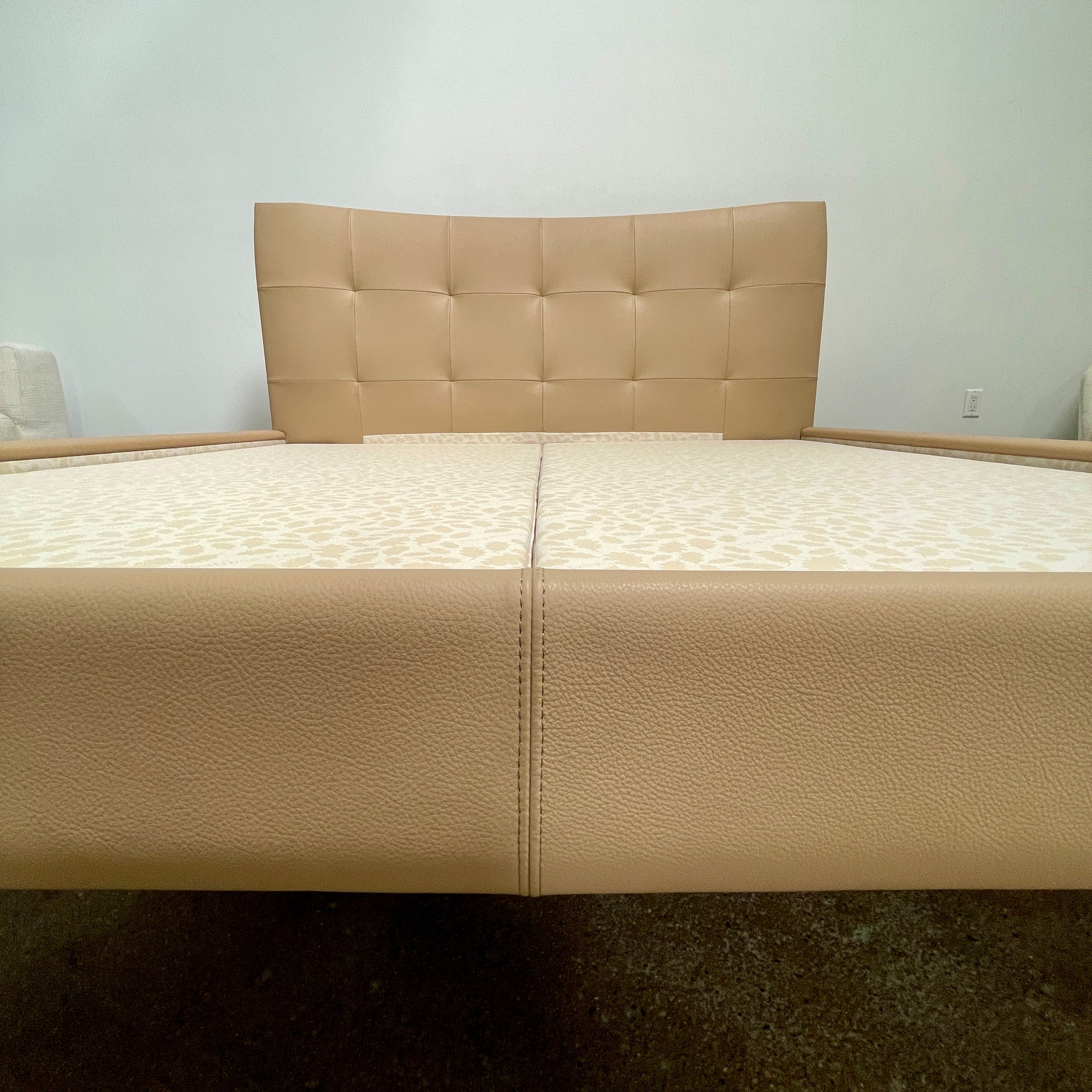 The Poltrona Frau Aurora Due King Bed, crafted by designer Tito Agnoli, boasts a minimalist and modern style with its beige tufted headboard set against a plain light gray wall.