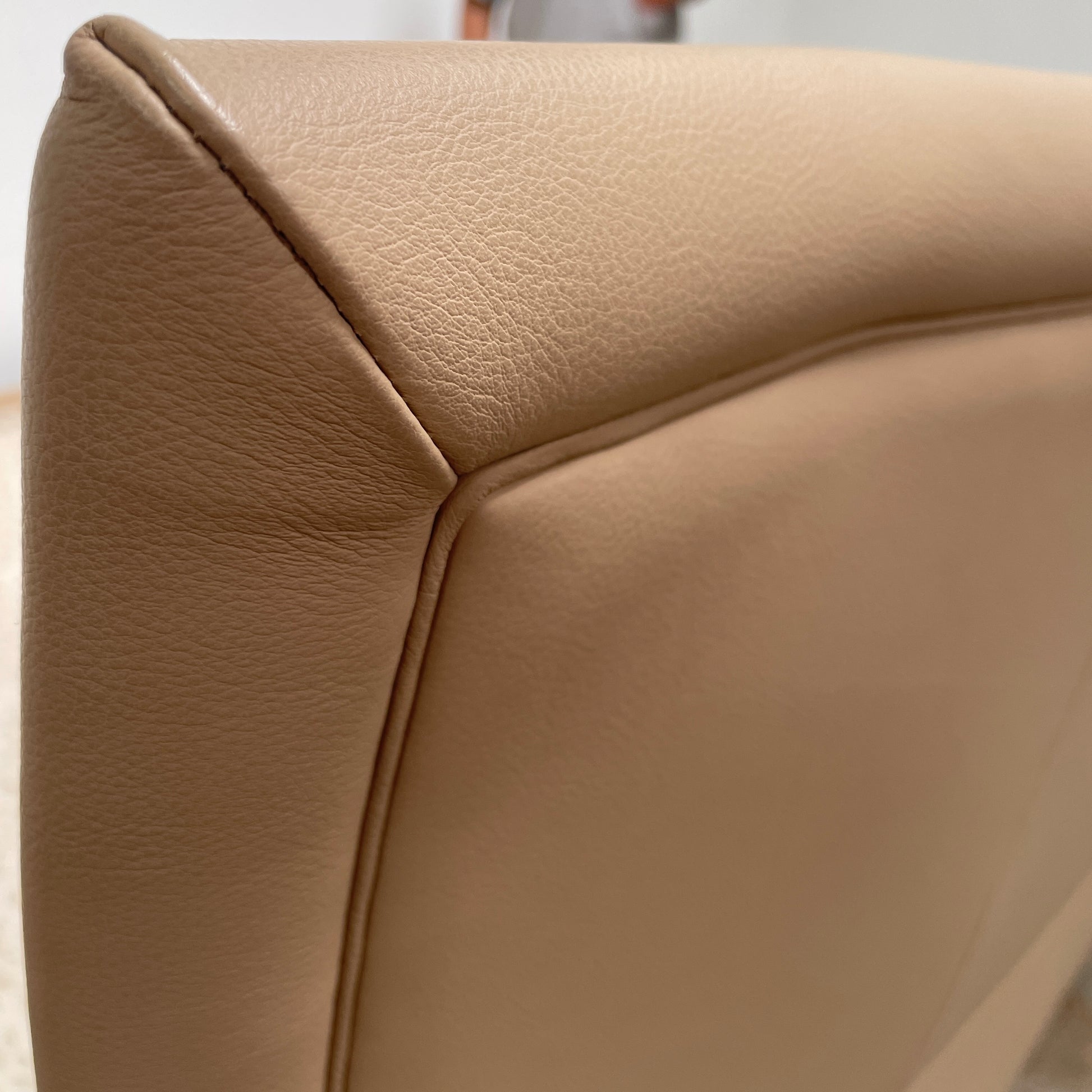 The Poltrona Frau Aurora Due King Bed, crafted by designer Tito Agnoli, boasts a minimalist and modern style with its beige tufted headboard set against a plain light gray wall.