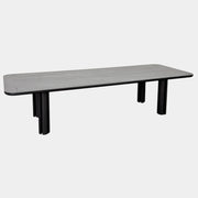 A rectangular black Porada Quadrifolgio Dining Table with rounded corners and four cylindrical legs stands on a brown floor against a plain white wall.