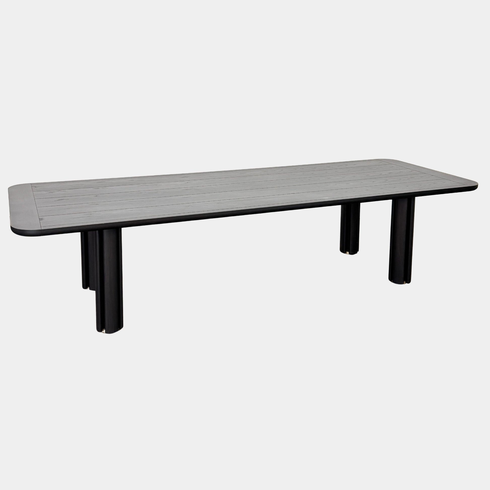 A rectangular black Porada Quadrifolgio Dining Table with rounded corners and four cylindrical legs stands on a brown floor against a plain white wall.
